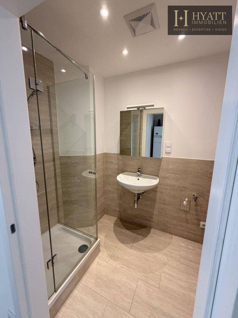 Modernes Badezimmer mit Duschkabine, Waschbecken, Spiegelschrank und beigefarbenen Fliesen.