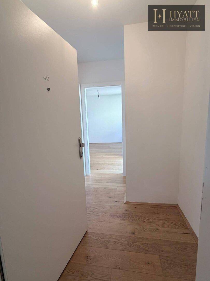 Eingangsbereich mit Holzboden und offener Tür, die den Blick in die helle Wohnung freigibt.