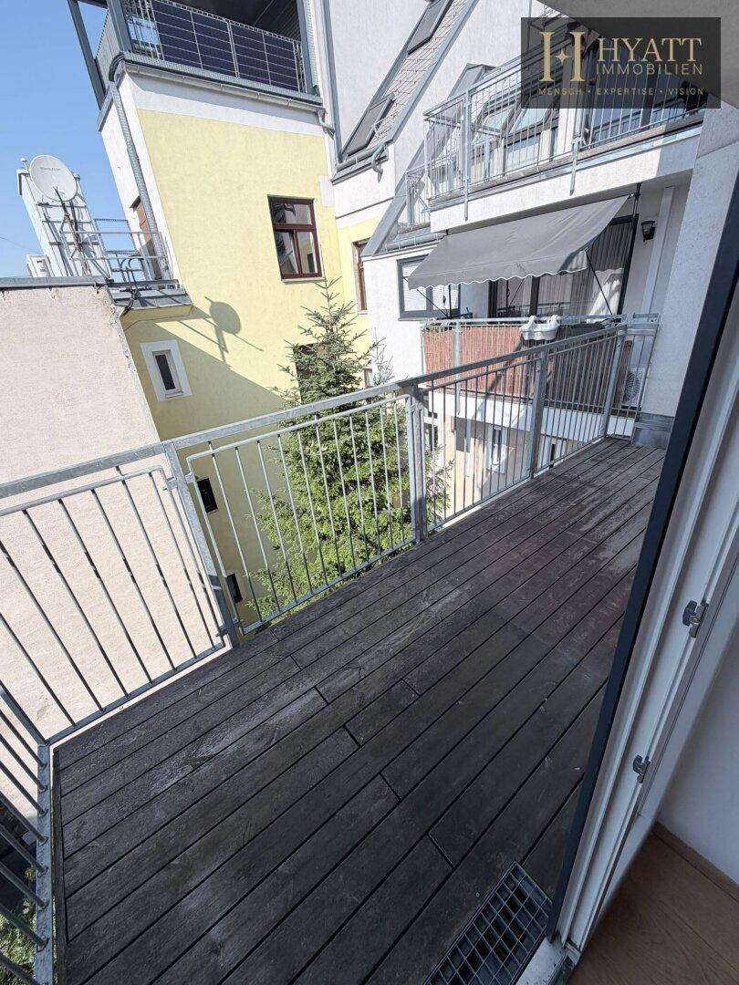 Kleiner Balkon mit Holzboden und Metallgeländer, bietet einen Blick auf die umliegenden Gebäude.