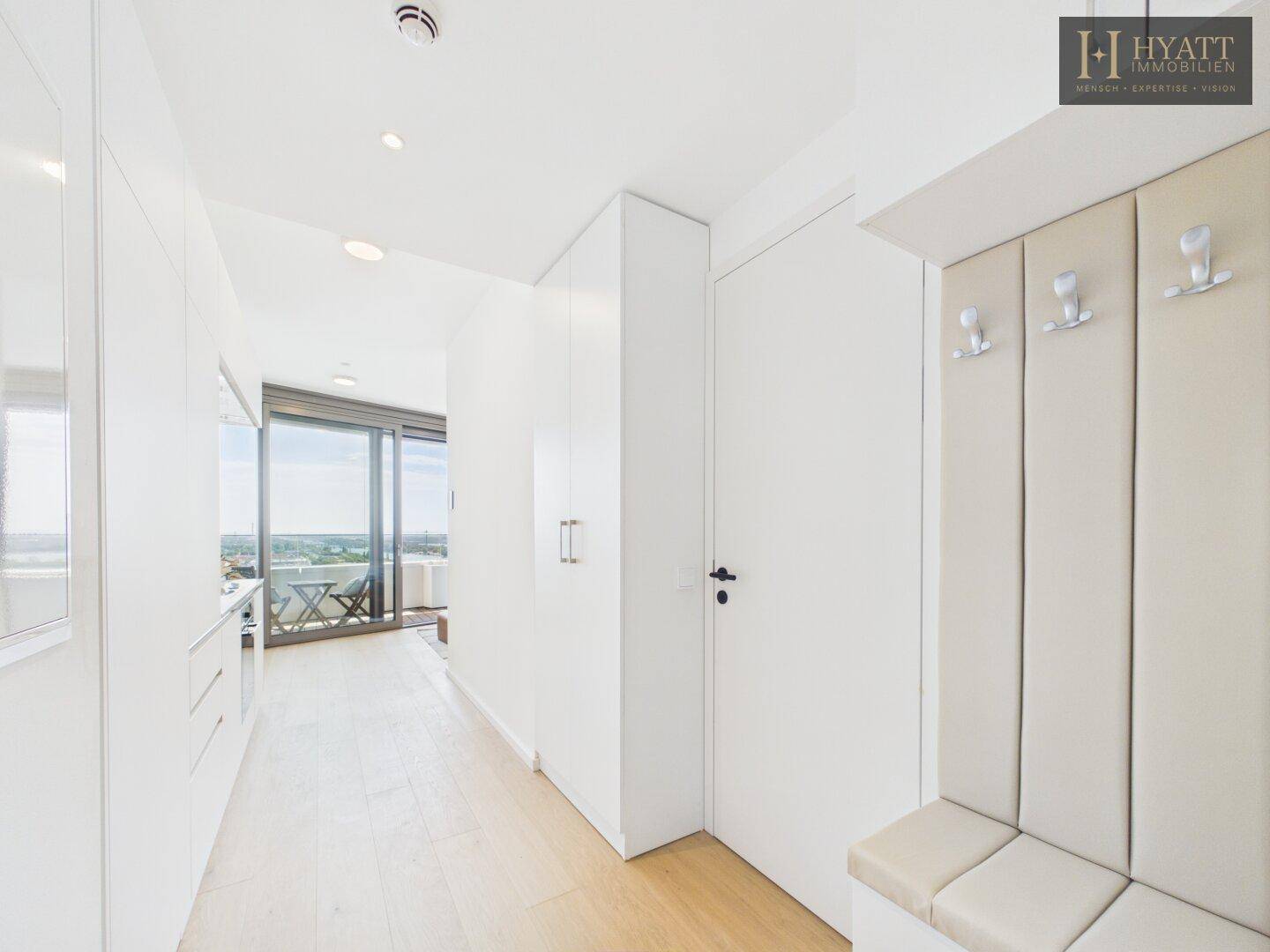 Heller Flur mit integrierten Schränken und Garderobe, der zum Wohnbereich mit Balkon führt.