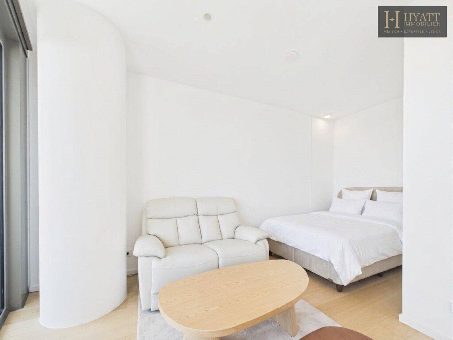 Helles Schlafzimmer mit Doppelbett, kleiner Couch und Holzboden, ideal für ein Studio-Apartment.