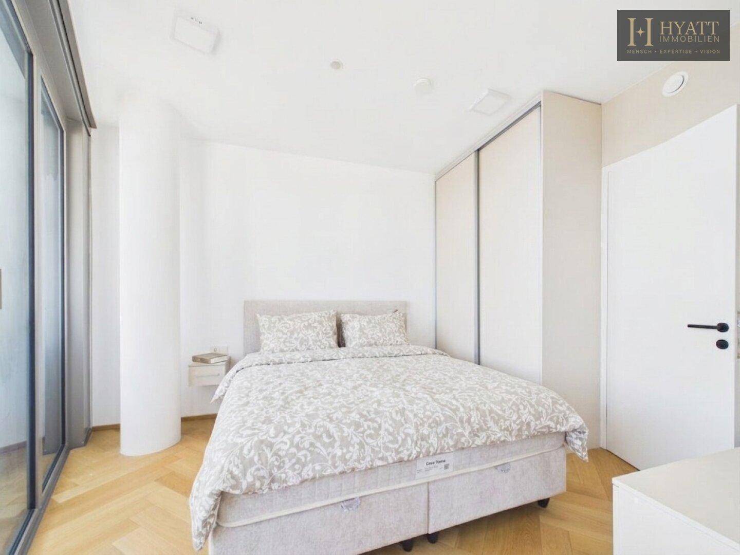 Helles Schlafzimmer mit Doppelbett, Einbauschrank und Parkettboden.
