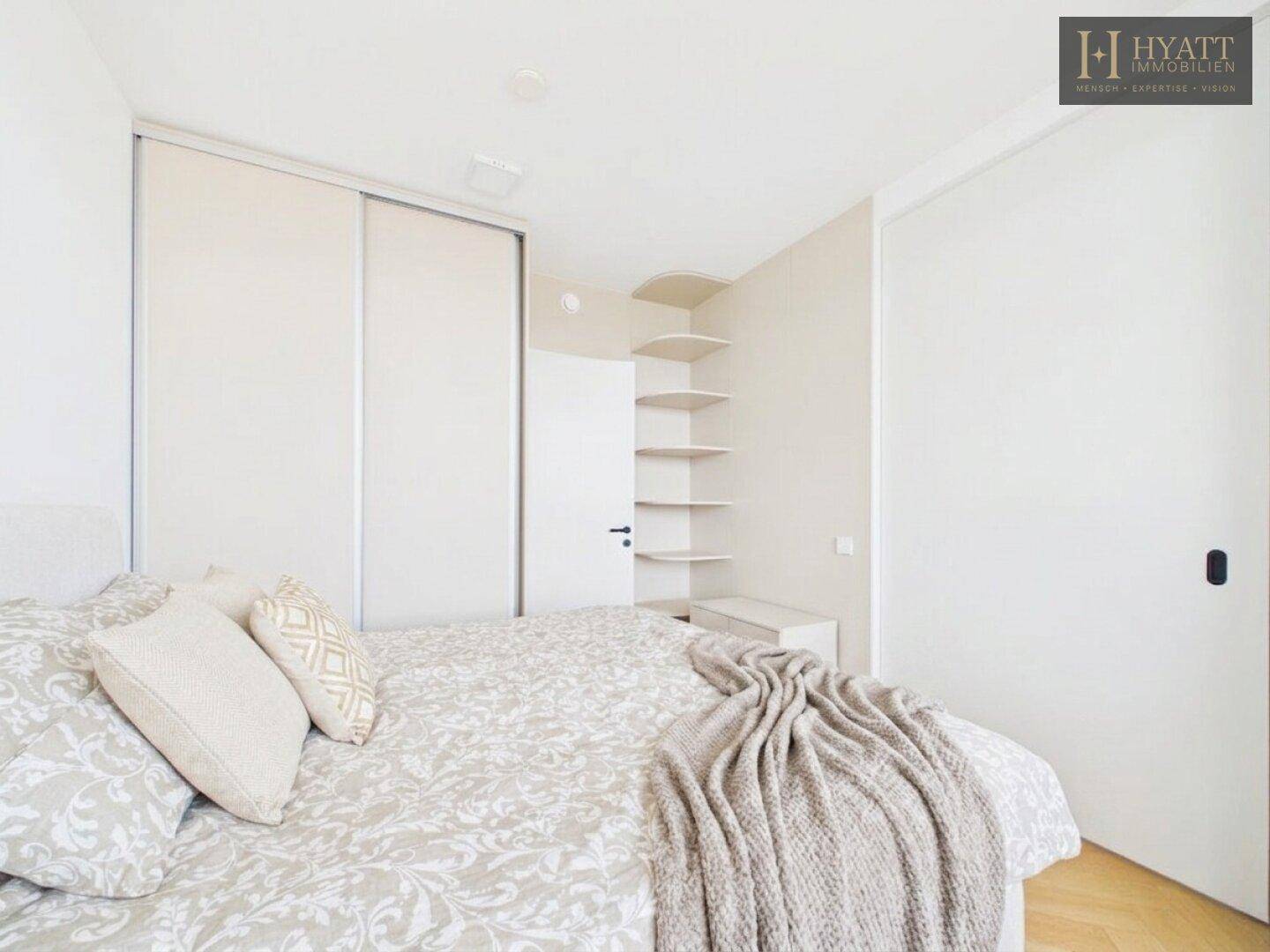 Schlafzimmer mit großem Bett, integrierten Schränken und dekorativen Wandregalen.