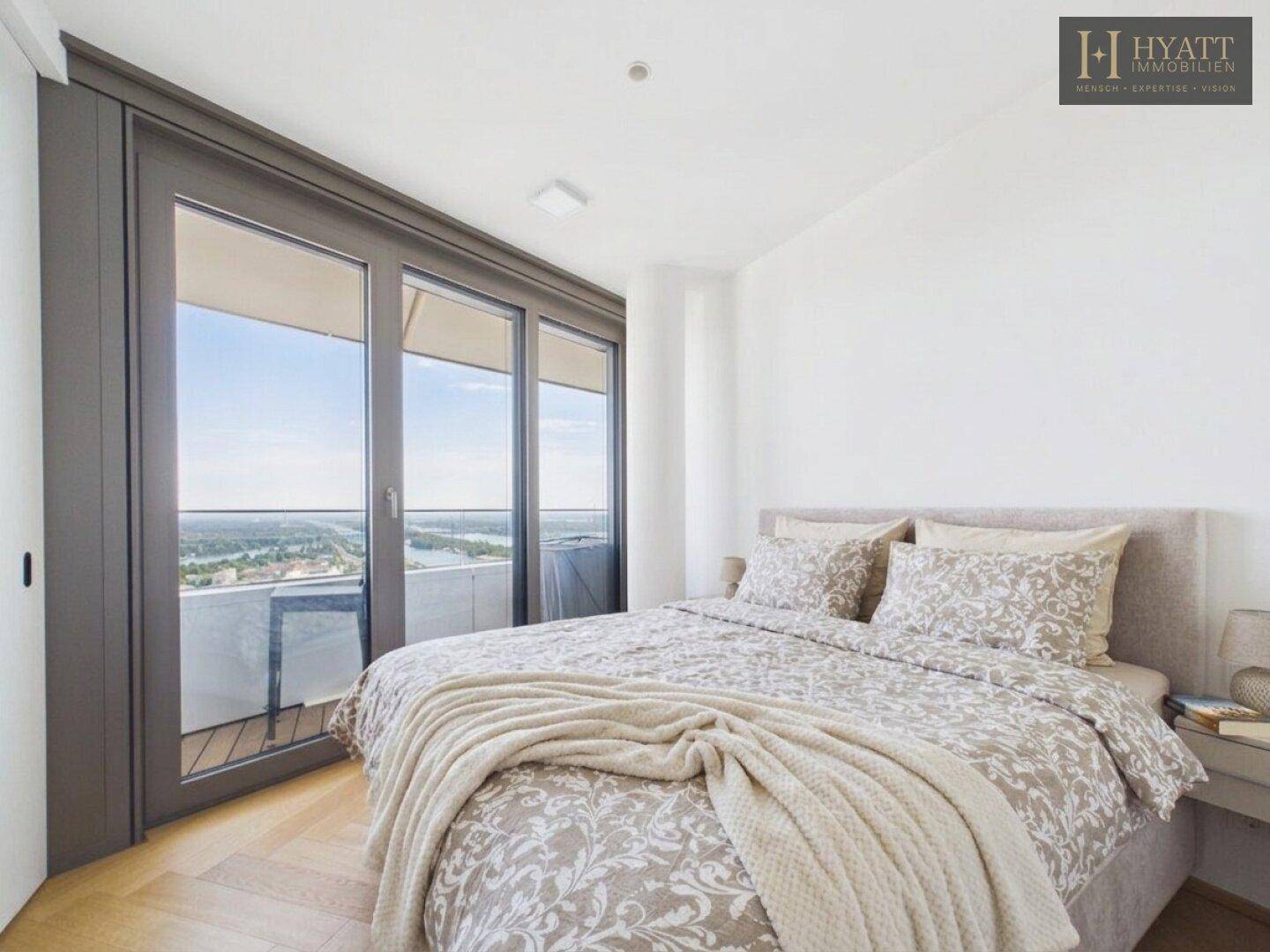 Schlafzimmer mit Balkonzugang, Doppelbett und weitem Ausblick über die Stadt.