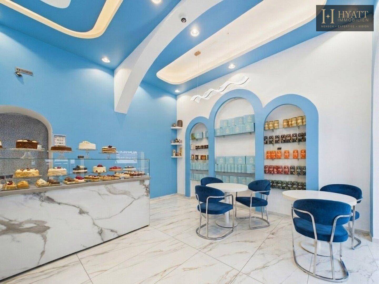 Innenansicht eines modernen Cafés mit blauen Stühlen, weißen Tischen und eleganten Marmor-Theken.
