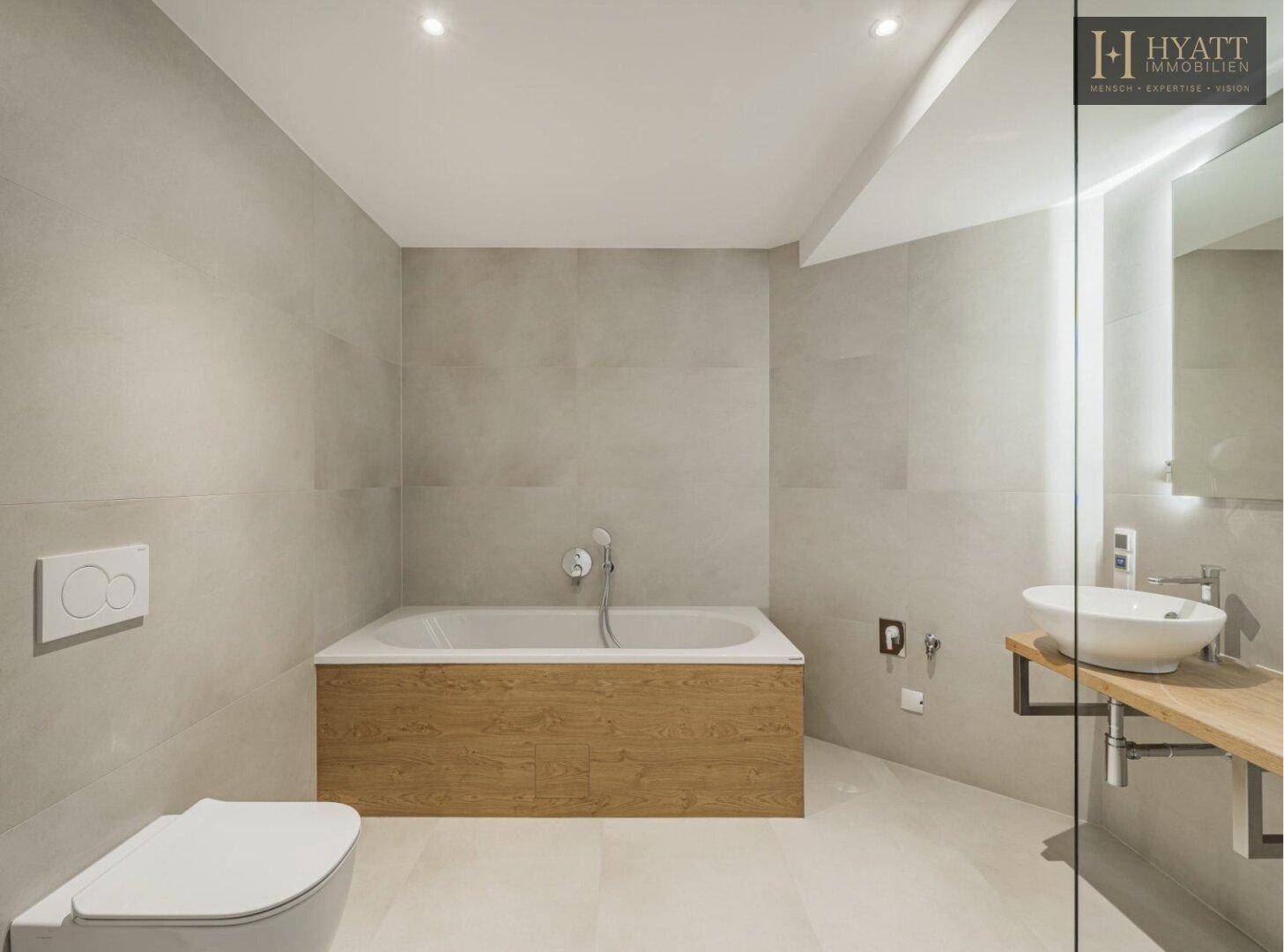 Modernes Badezimmer mit hellgrauen Fliesen, Badewanne, wandhängendem WC und stilvollem Einzelwaschbecken.