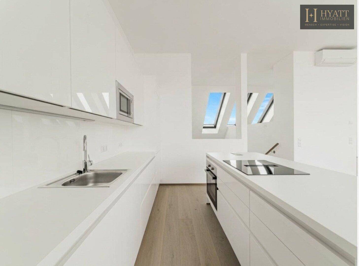 Moderne weiße Einbauküche mit Kochinsel, integrierten Geräten und Holzboden unter Dachfenstern.