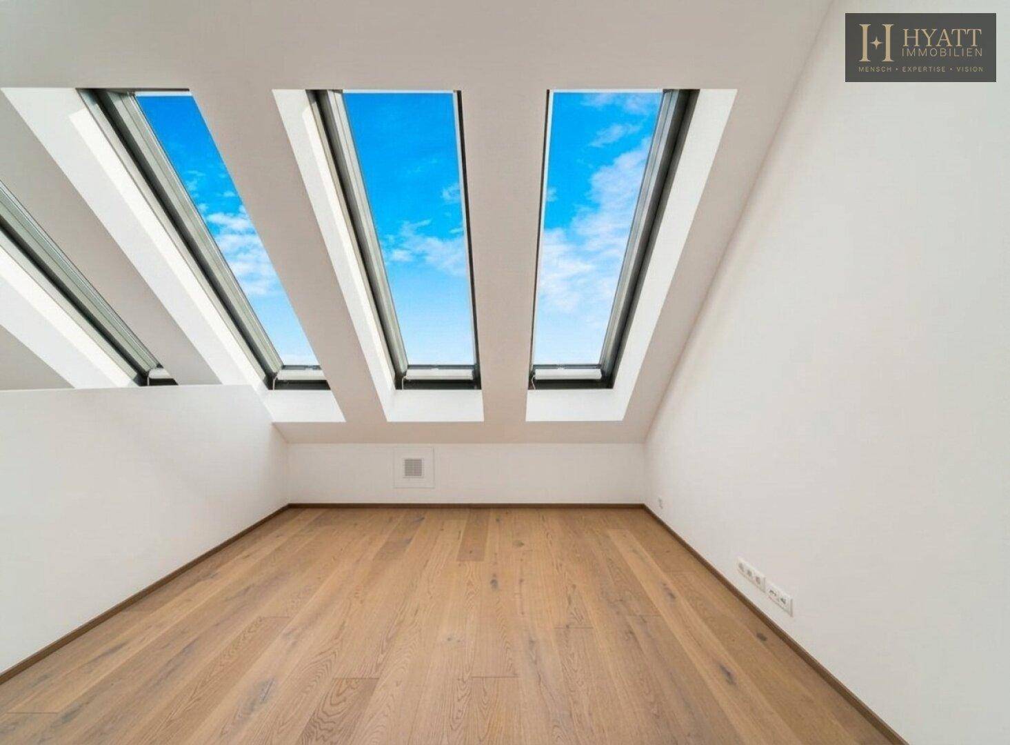 Helles Zimmer mit Holzboden, weißen Wänden und drei großen Dachfenstern für viel Tageslicht.