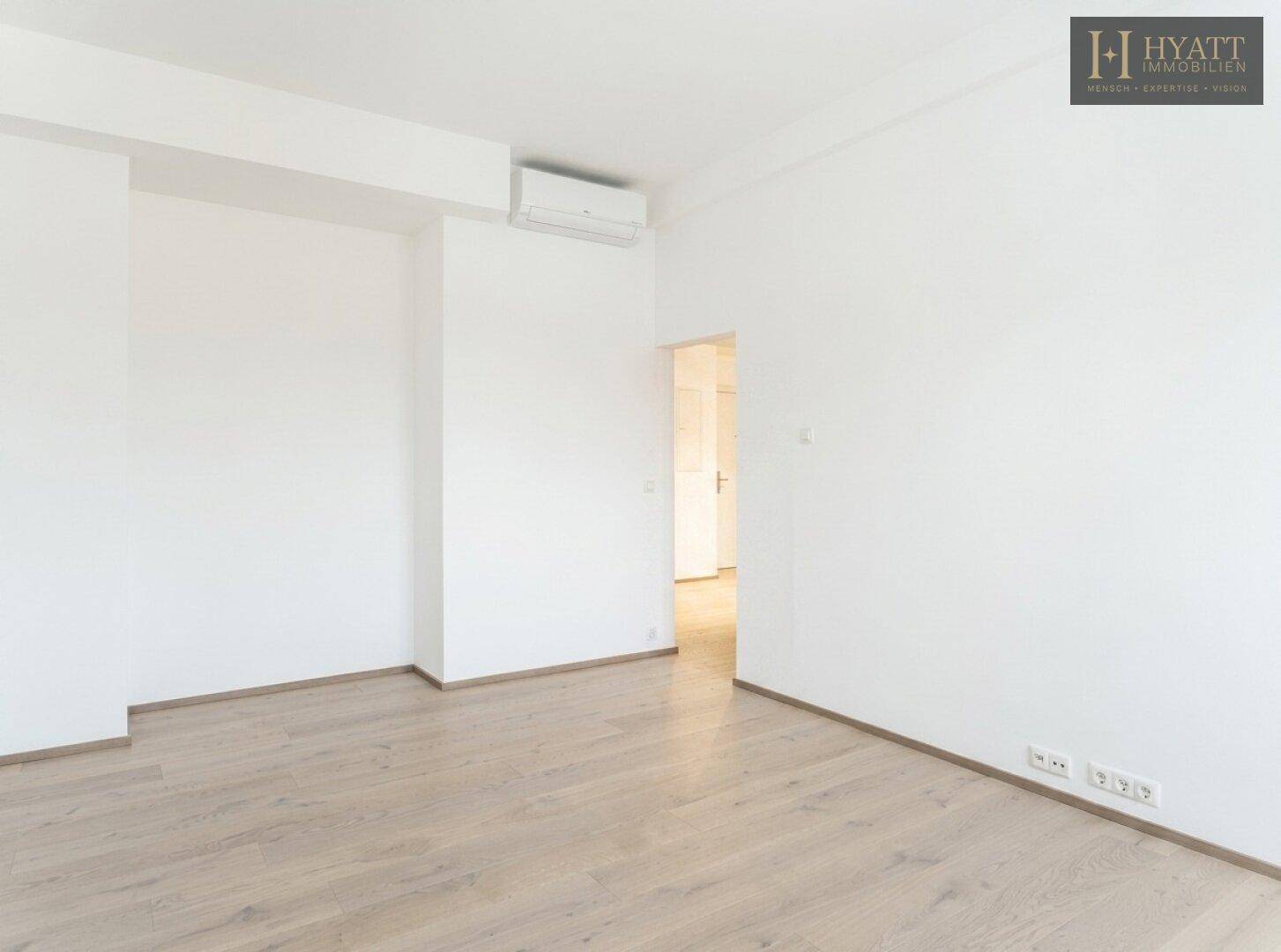 Leeres Zimmer mit Holzboden, weißen Wänden und einer Klimaanlage, bereit zur individuellen Gestaltung.