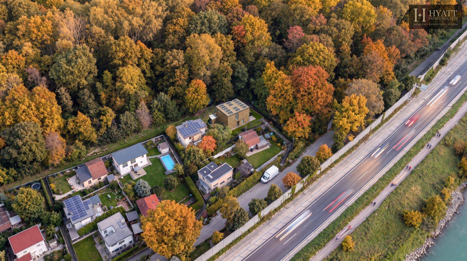 Luftaufnahme einer Wohnsiedlung mit modernen Häusern, umgeben von herbstlichen Bäumen und einer Straße.
