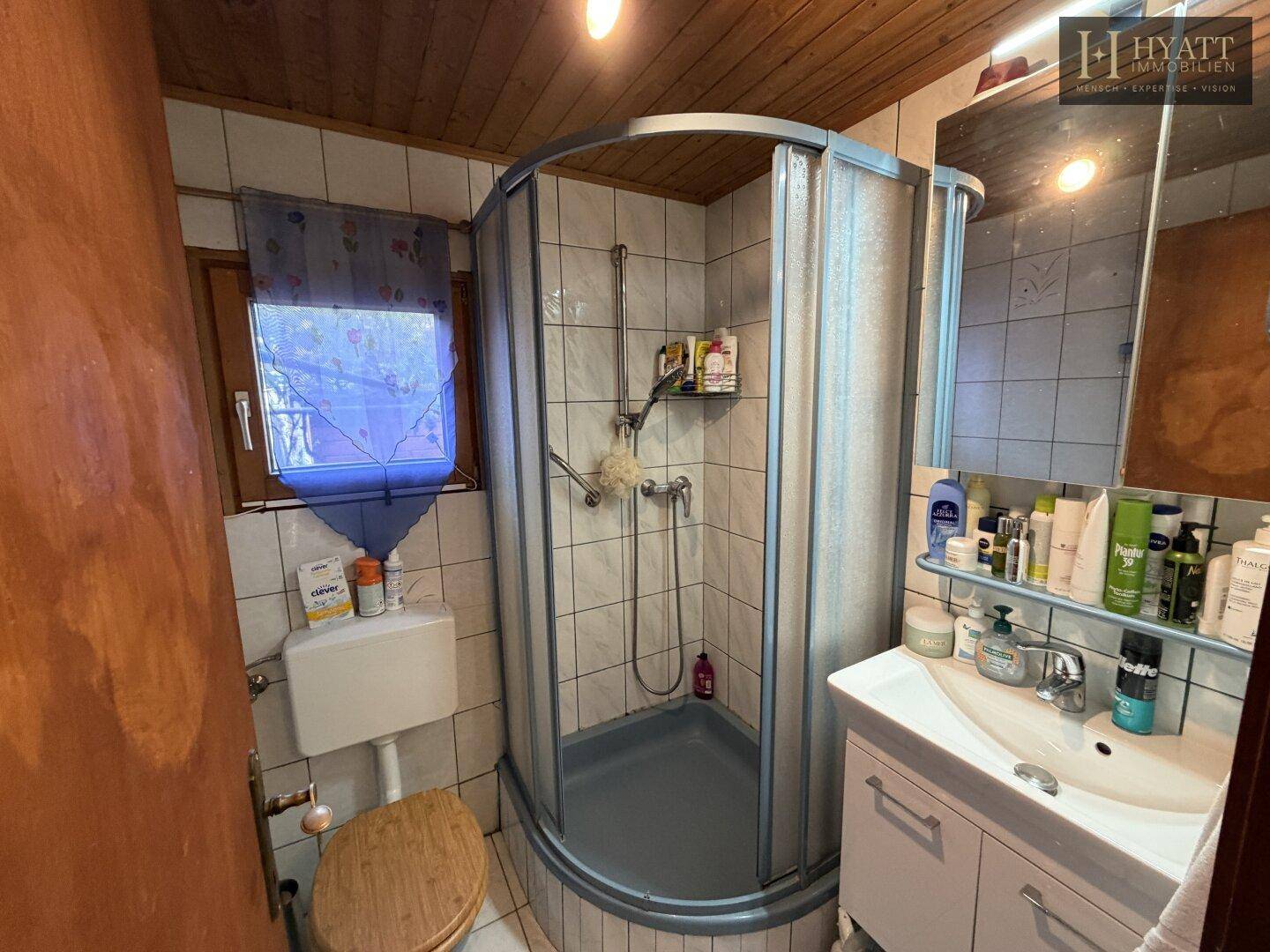 Kleines Badezimmer mit Eckdusche, WC und Waschbecken, hell gefliest.