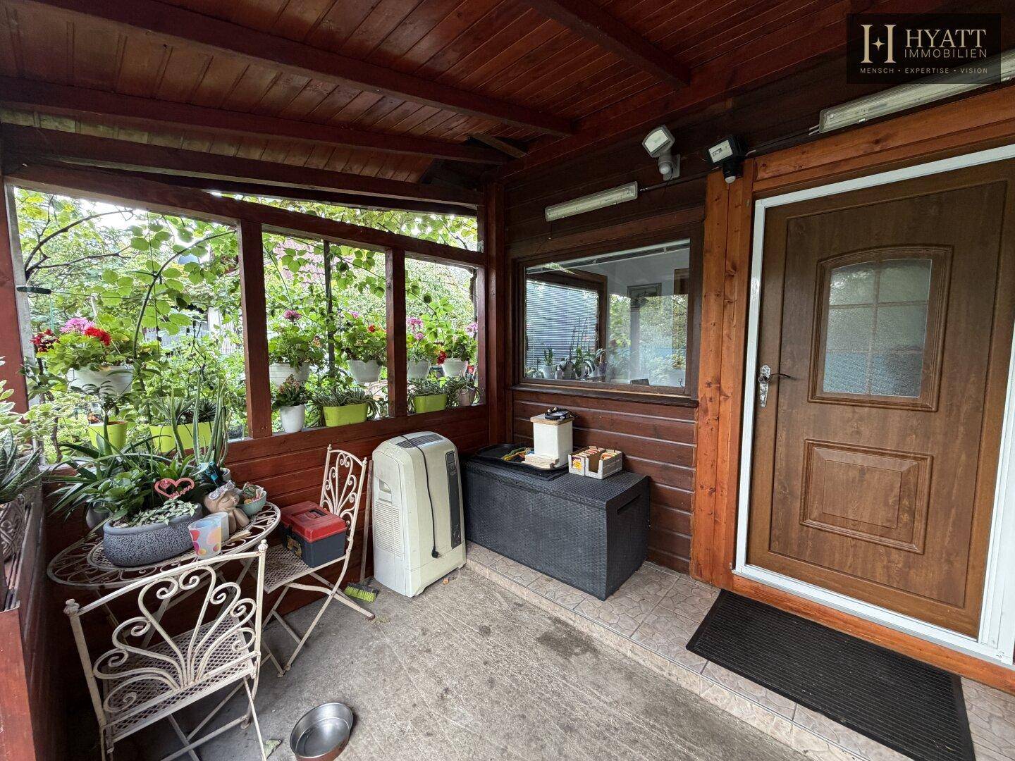 Überdachter Eingangsbereich mit Veranda und dekorativen Pflanzen, einladend gestaltet.