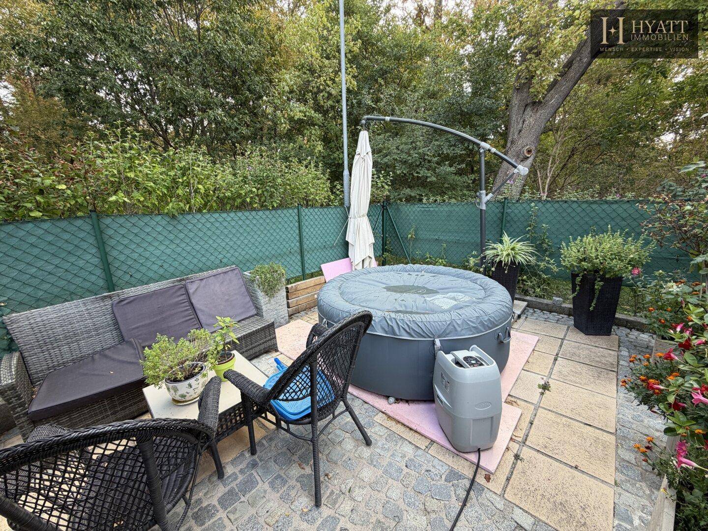 Gemütliche Terrasse mit Whirlpool und Sitzgelegenheiten im Freien, umgeben von Grün.