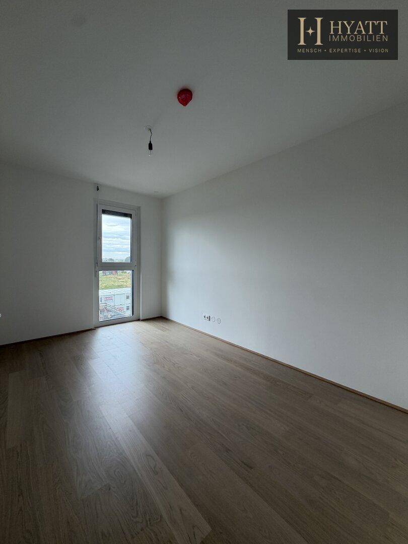 Helles, leeres Zimmer mit Holzboden und großem Fenster, bereit zur individuellen Gestaltung.