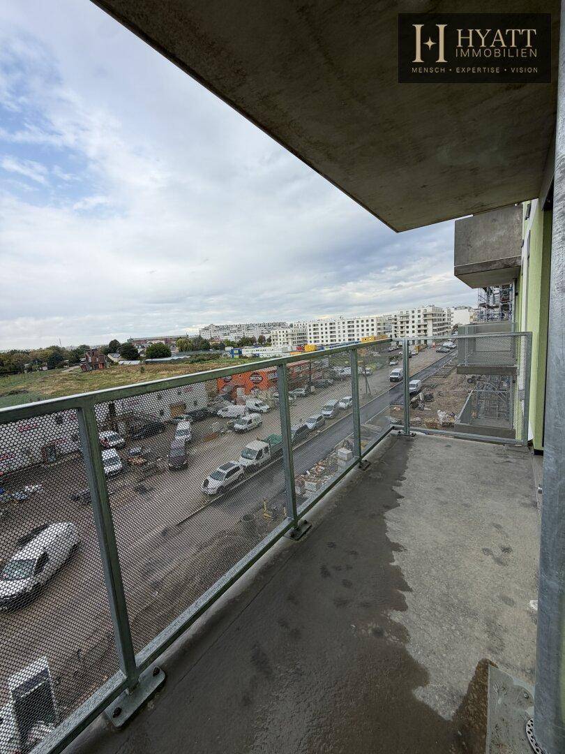 Leerer Balkon mit Glasgeländer und Blick auf die Umgebung und eine Baustelle.