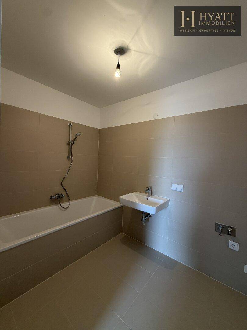 Helles Badezimmer mit Badewanne, Waschbecken und WC, in neutralen Beigetönen gefliest.