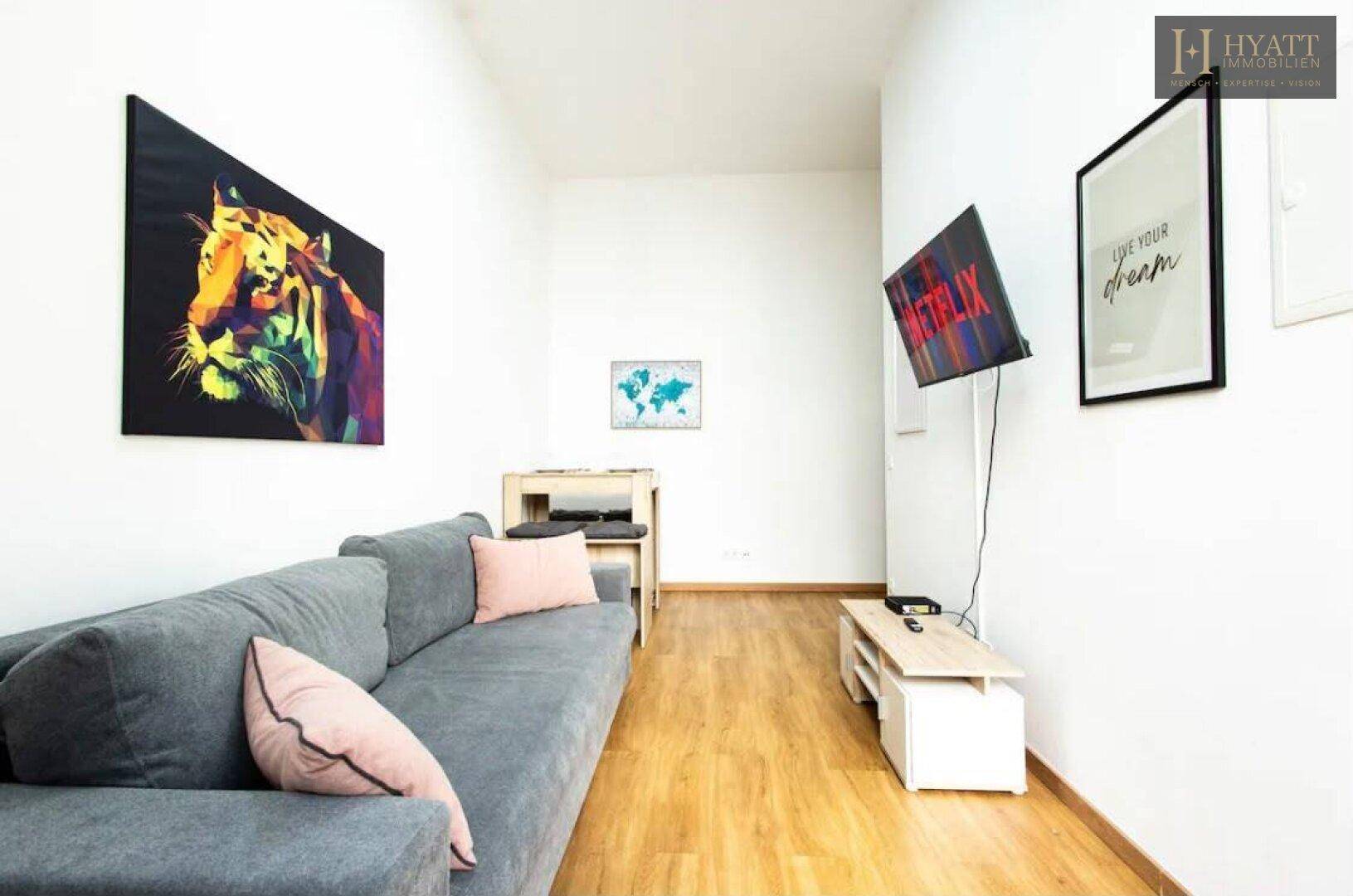 Helles Wohnzimmer mit bequemem Sofa, Wandfernseher und Holzboden, ideal zum Entspannen.