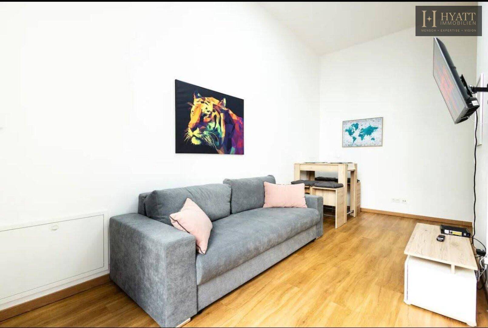 Gemütliches Wohnzimmer mit grauem Sofa, Holzboden und Wandfernseher für entspannte Abende.