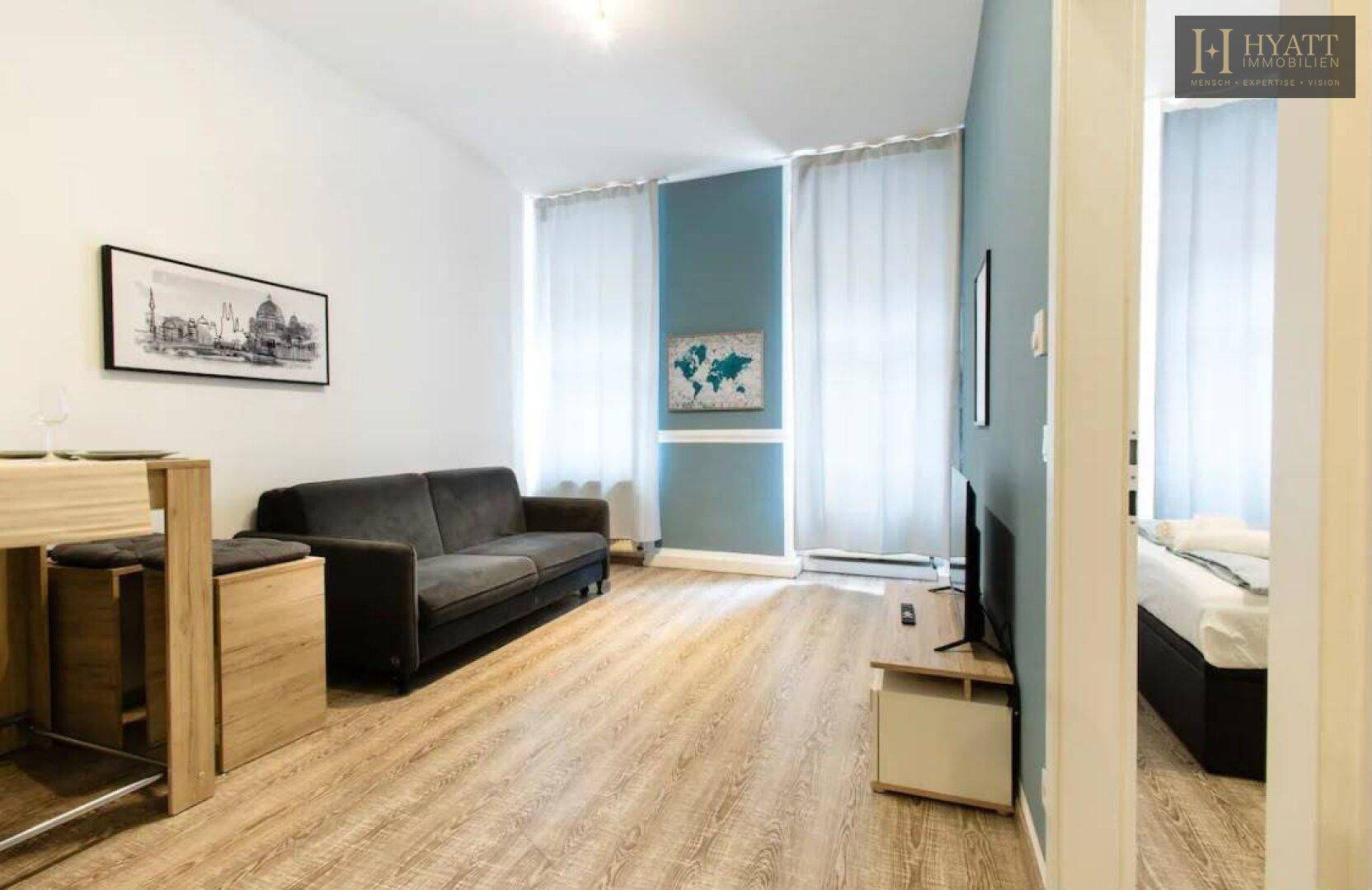 Geräumiges Wohnzimmer mit dunklem Sofa, Holzboden und großen Fenstern mit Vorhängen.