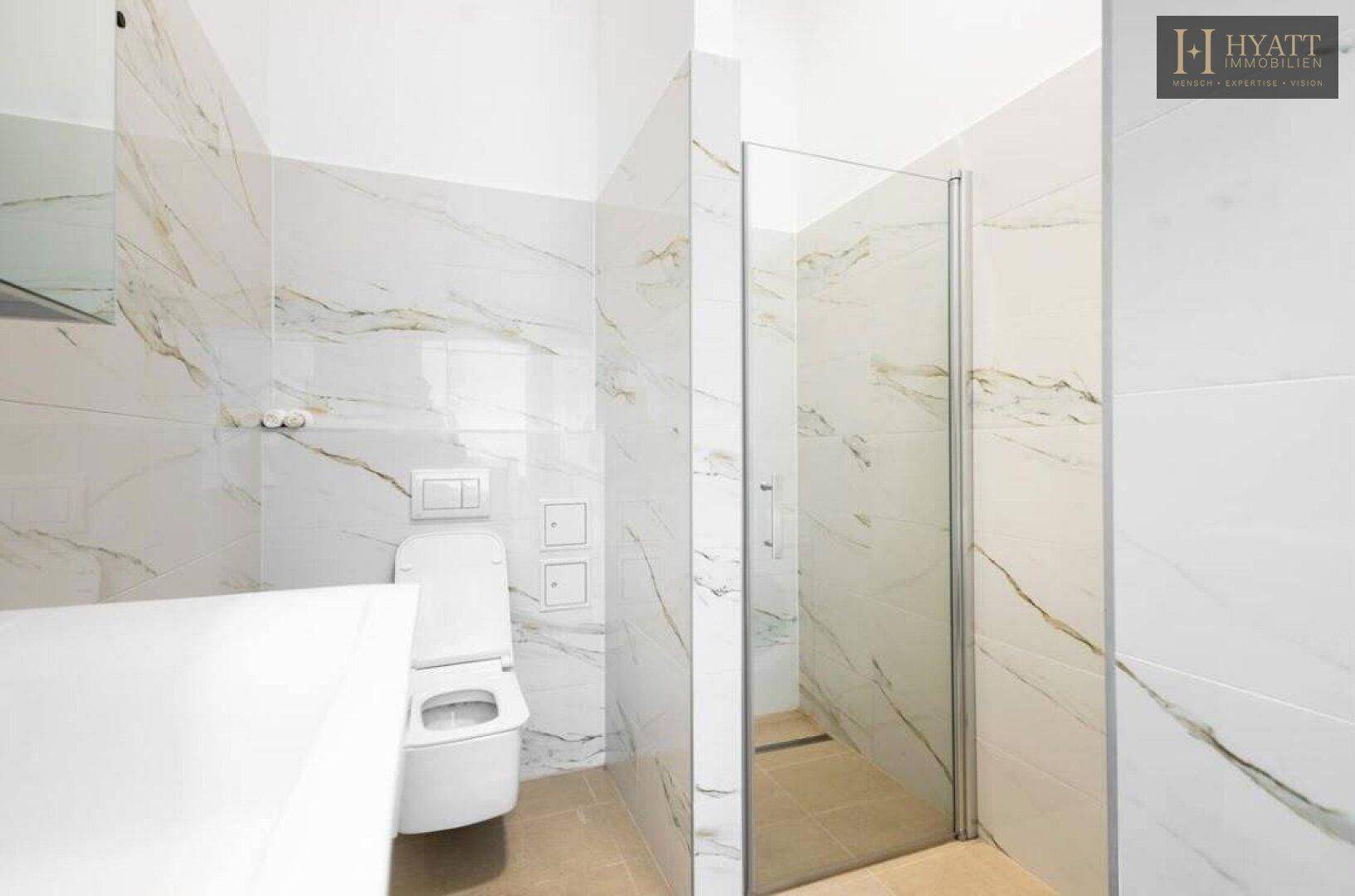 Elegantes Badezimmer mit großen Marmorfliesen, Duschbereich und wandhängendem WC.