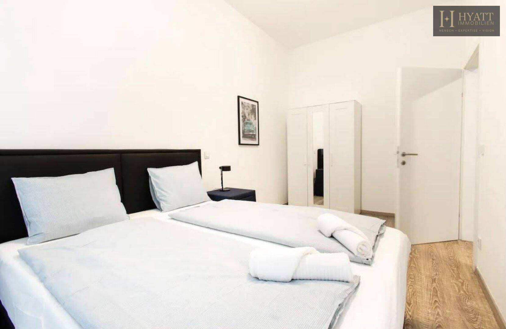 Helles Schlafzimmer mit Doppelbett, Nachttischen und weißem Kleiderschrank mit Spiegeltür.