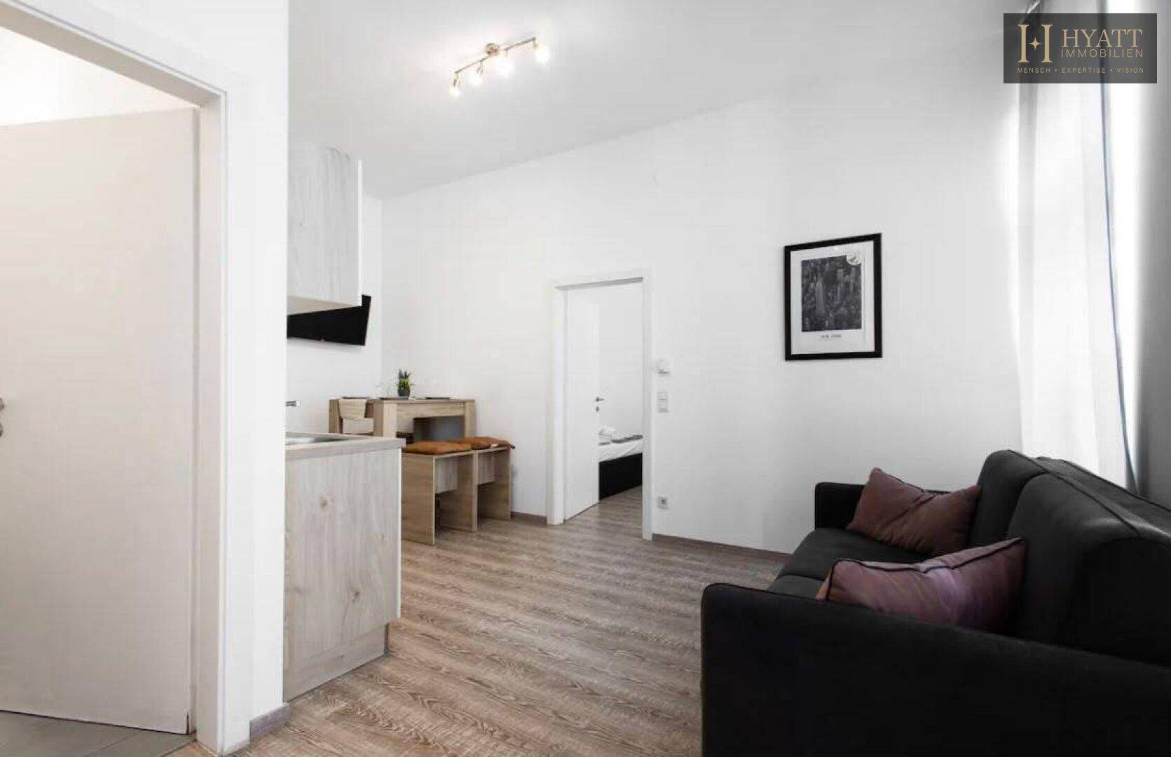 Heller Wohnbereich mit Sofa, Esstisch und Blick auf eine offene Tür zum Schlafzimmer.