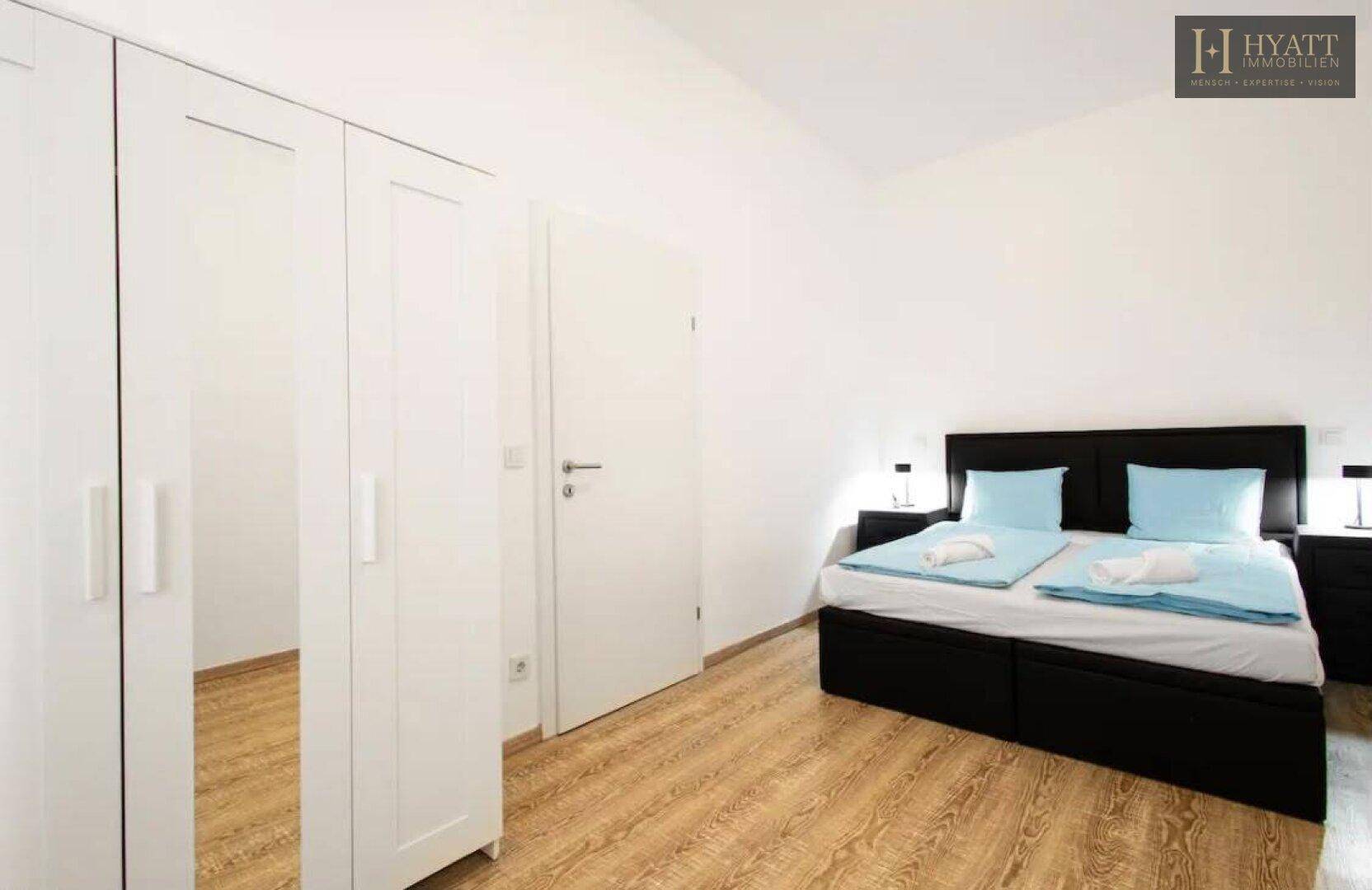 Helles Schlafzimmer mit Doppelbett, Nachttischen und weißem Kleiderschrank mit Spiegeltüren.
