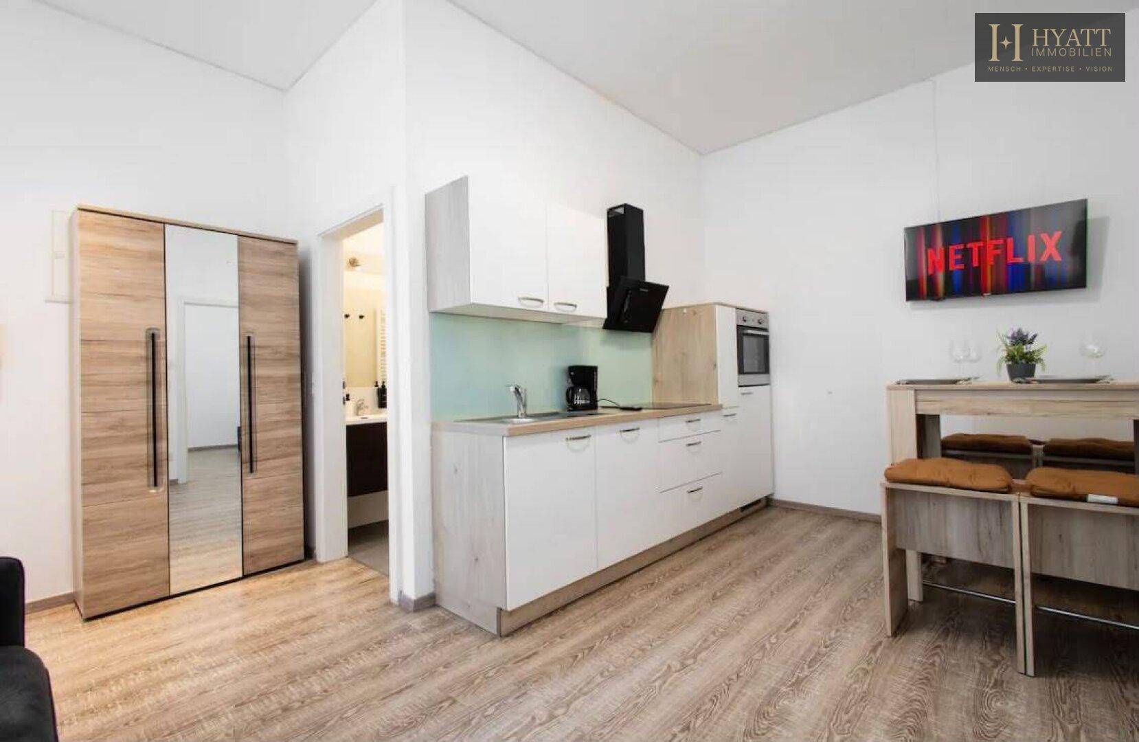 Offener Wohnbereich mit Küchenzeile, Esstisch und Zugang zum Badezimmer.