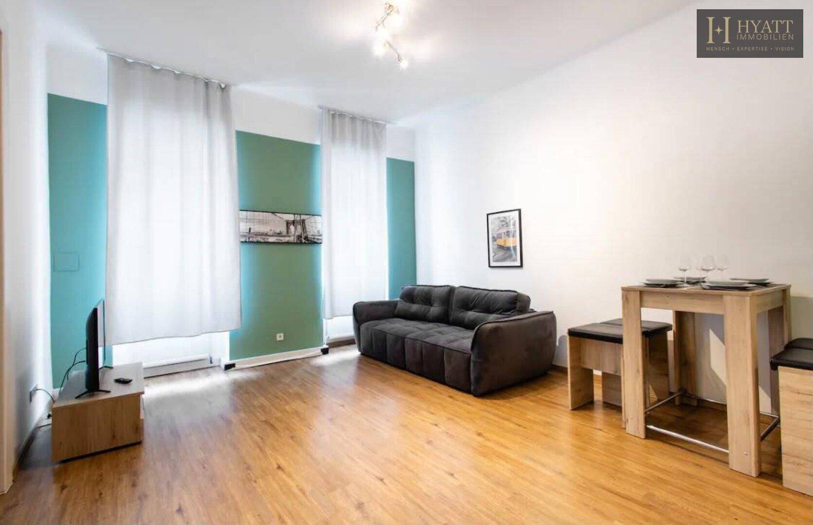 Helles Wohnzimmer mit Sofa, Esstisch und Holzboden, akzentuiert durch grüne Wandstreifen.