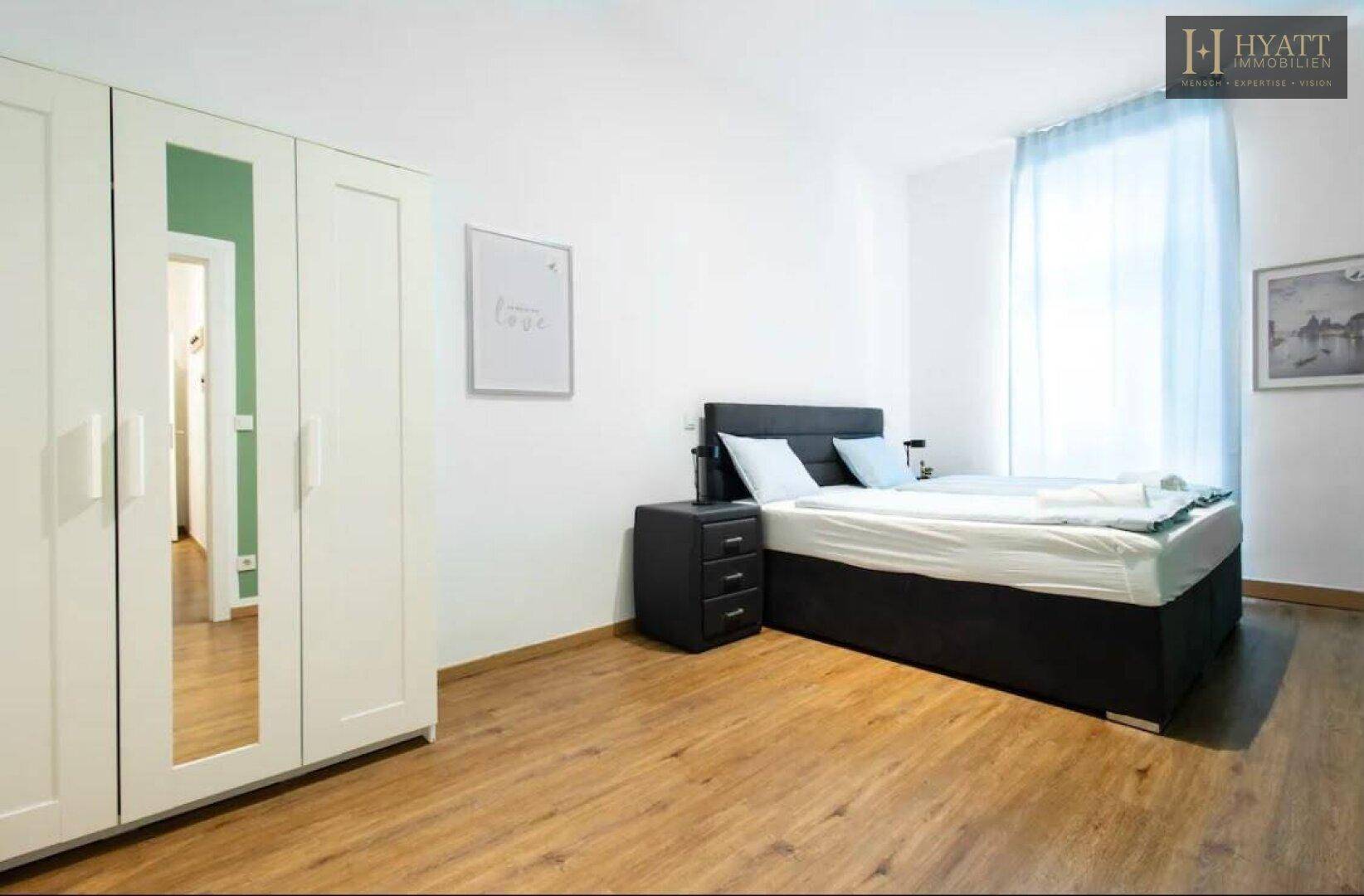 Helles Schlafzimmer mit Doppelbett, Nachttisch und weißem Kleiderschrank mit Spiegeltüren.