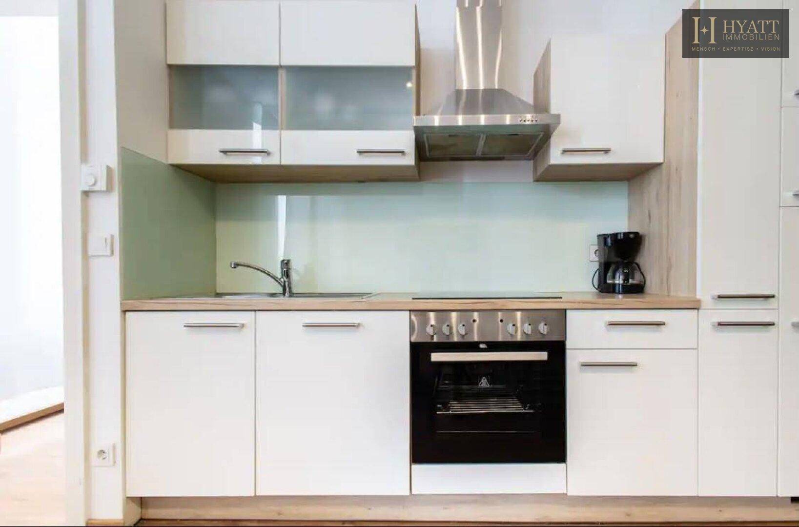 Nahaufnahme der modernen Einbauküche mit weißen Schränken, Holztheke, integriertem Backofen und Dunstabzugshaube.