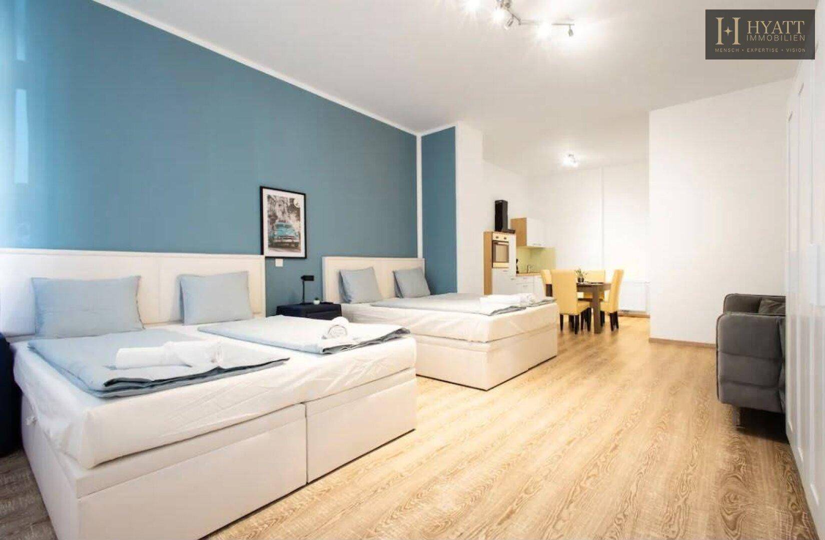 Offenes Studio-Apartment mit Schlafbereich, Wohnbereich und kleiner Küchenzeile im Hintergrund, sehr hell.