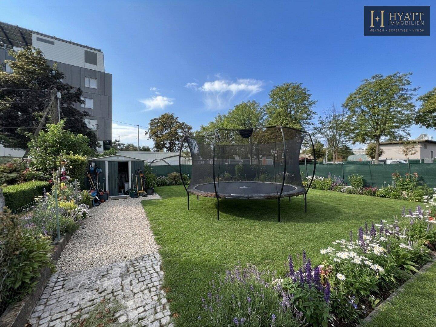 Großer Garten mit Rasenfläche, Trampolin und einem praktischen Gartenschuppen am Rand.