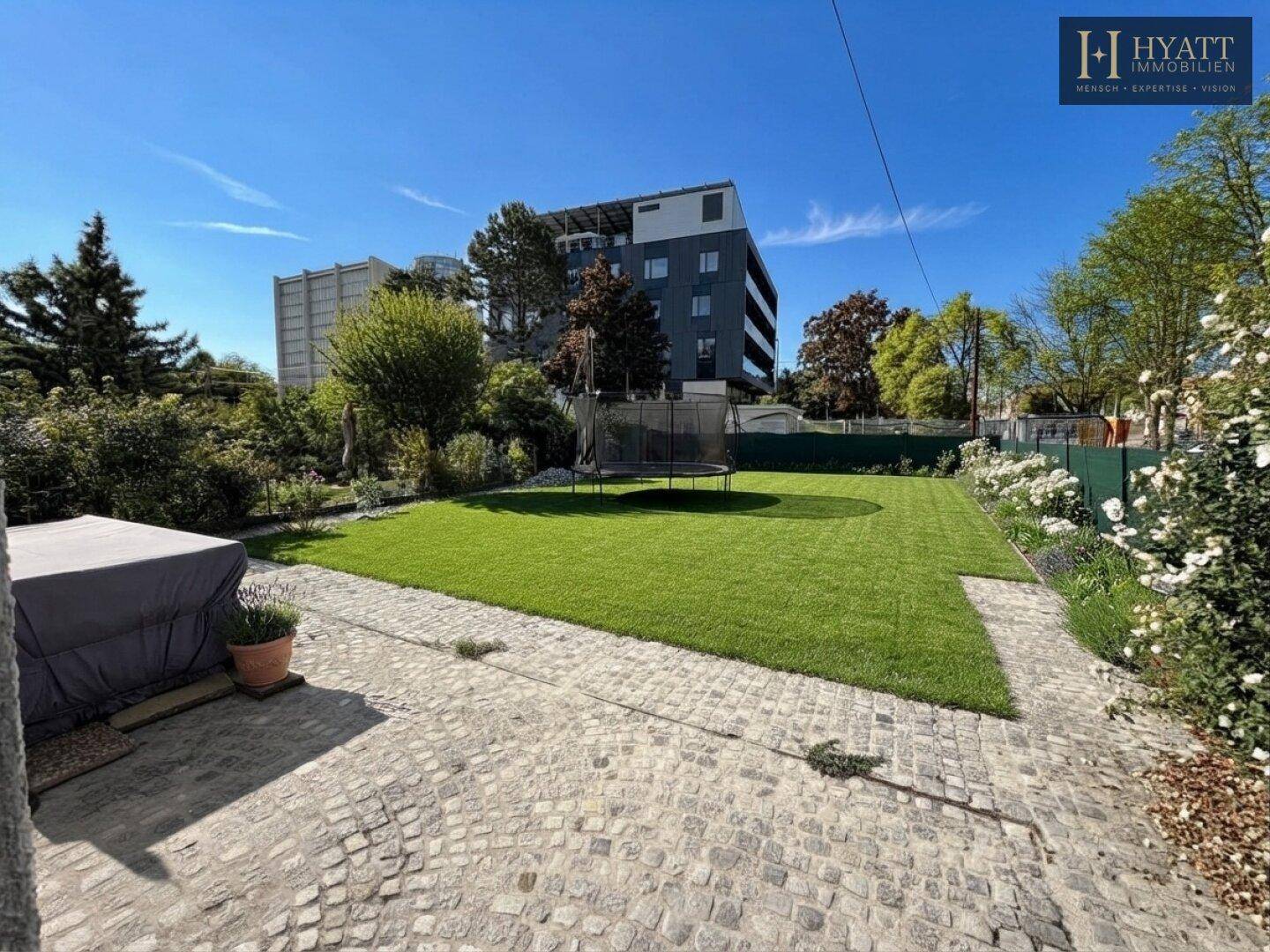 Gepflegter Garten mit frischem Rasen, Trampolin und Blick auf ein modernes Gebäude.