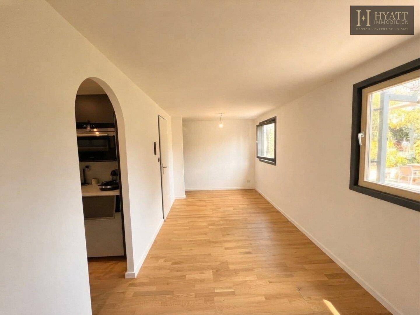 Wohnbereich mit Holzboden und einem Durchgang zu einer kleinen, separaten Küchenzeile.