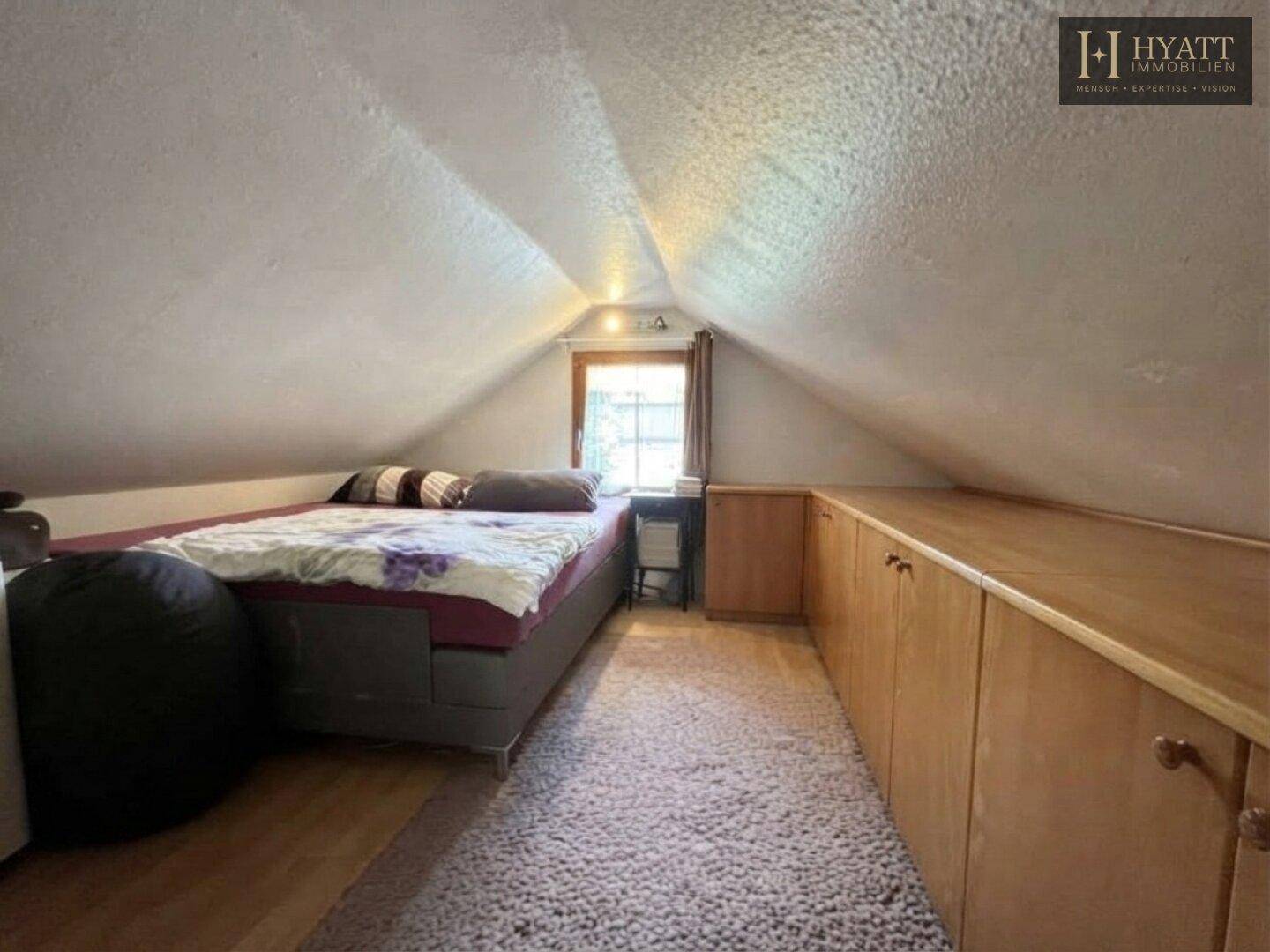 Gemütliches Schlafzimmer im Dachgeschoss mit schrägen Wänden und Holzboden.