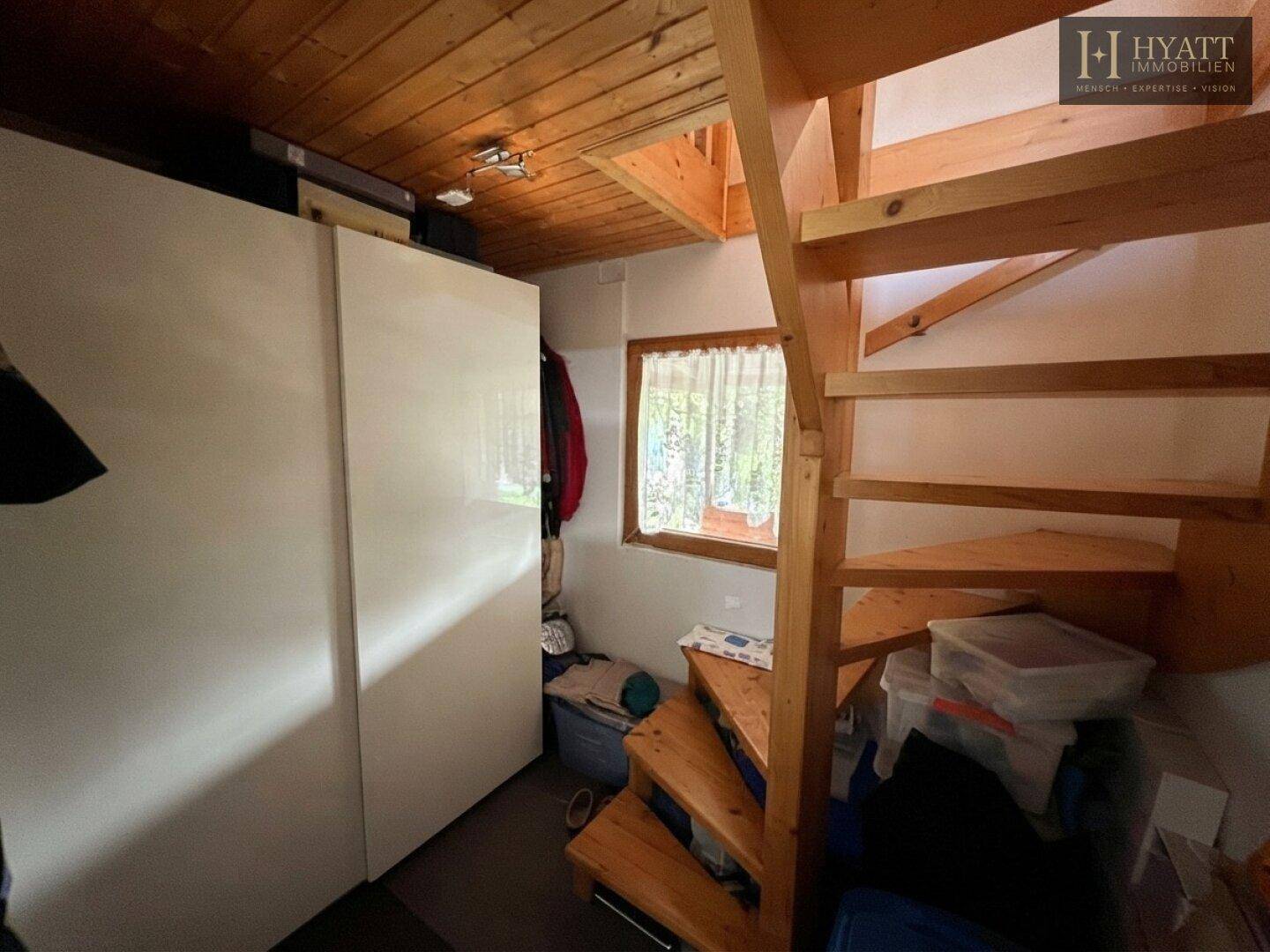 Hölzerne Wendeltreppe führt in den oberen Bereich, daneben ein weißer Kleiderschrank.