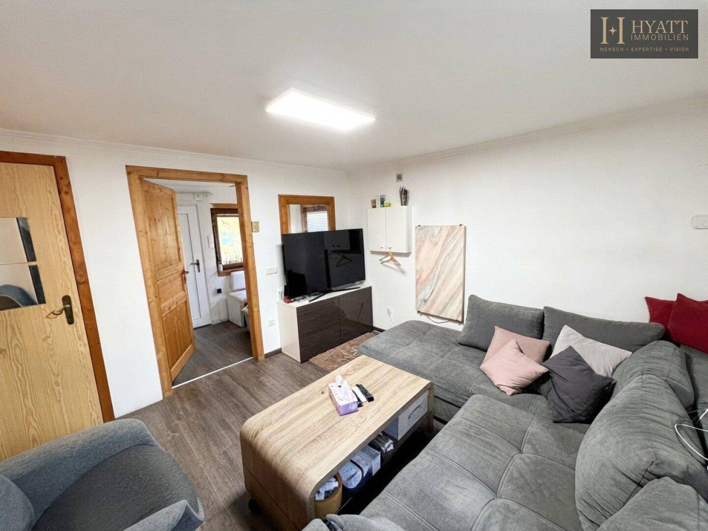 Wohnzimmer mit Fernseher und Zugang zu weiteren Räumen, ausgestattet mit Laminatboden.