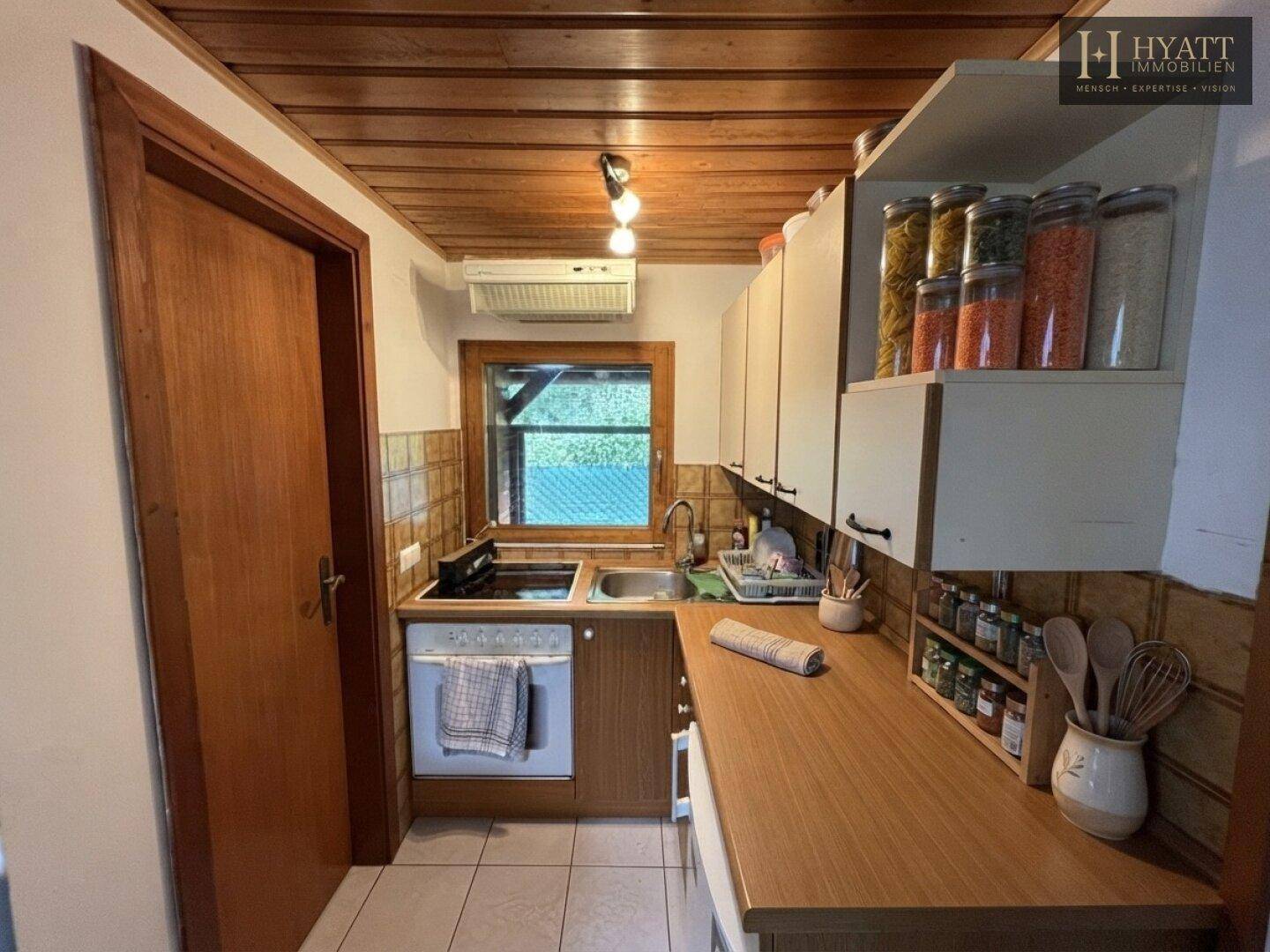 Funktionale Küchenzeile mit Holzdecke und Fenster, ausgestattet mit grundlegenden Geräten.