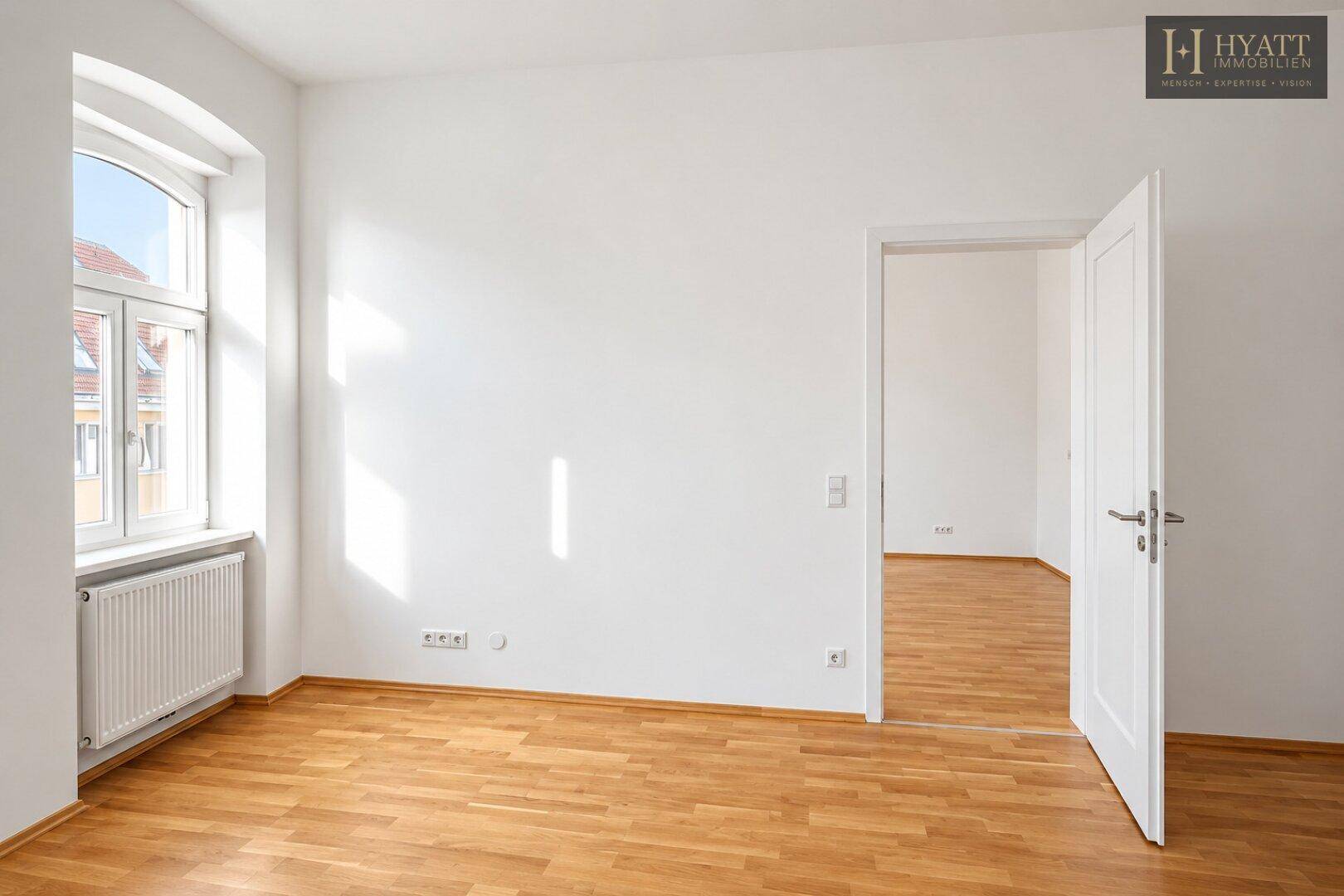 Helles, leeres Zimmer mit Parkettboden und einem großen Fenster, das viel natürliches Licht in den Raum bringt.