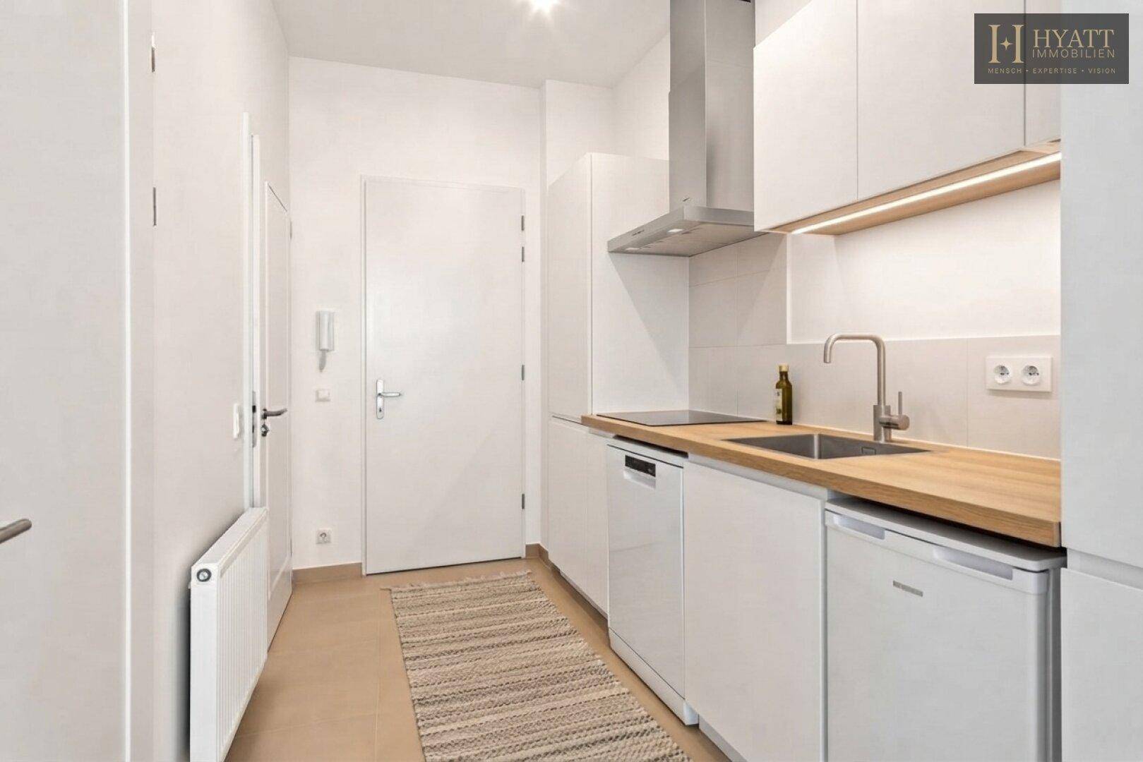 Moderne, kompakte Küche mit weißen Schränken, Holzarbeitsplatte und integrierten Geräten, ideal für kleine Räume.
