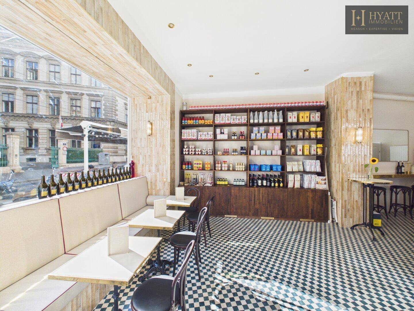Innenansicht eines Cafés mit kariertem Boden, Sitzbänken und Regalen voller Produkte.