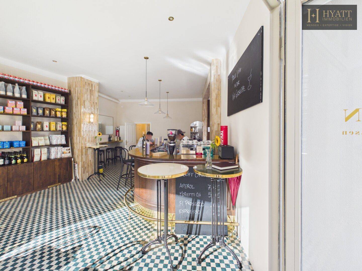 Blick auf die Theke eines Cafés mit Barhockern und Regalen im Hintergrund, durch die Tür gesehen.