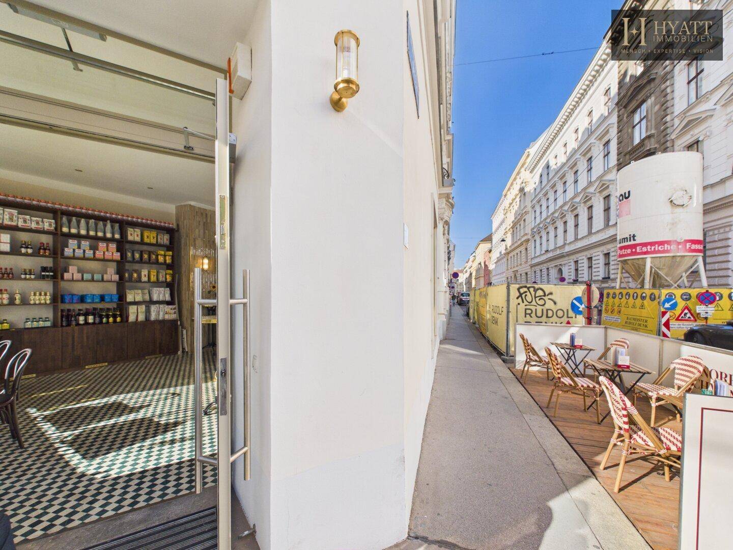 Seitenansicht des Cafés mit offener Tür, Außenterrasse und Blick auf die belebte Straße.