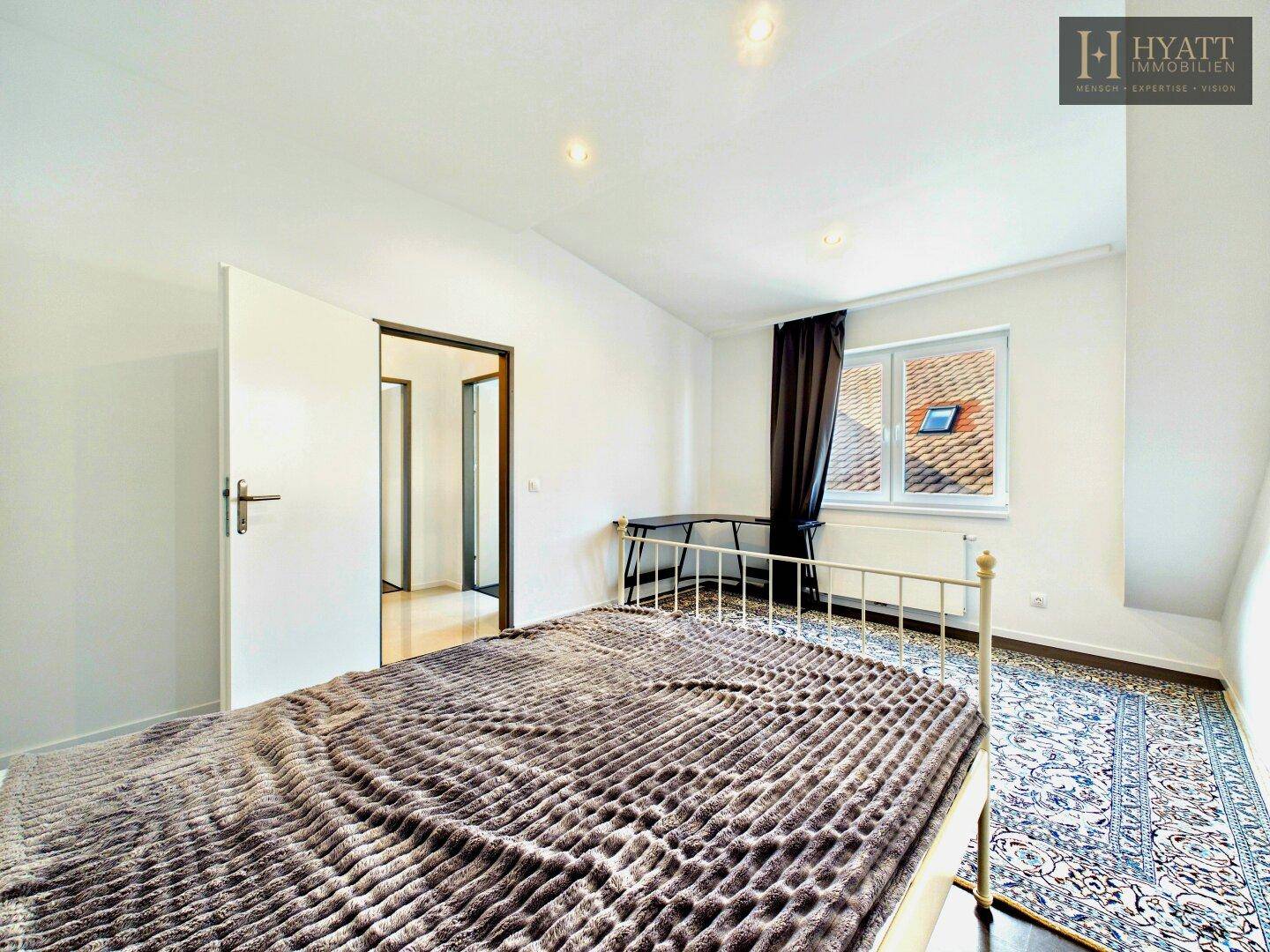 Gemütliches Schlafzimmer im Dachgeschoss mit Bett, Teppich und Fenster mit Blick nach draußen.