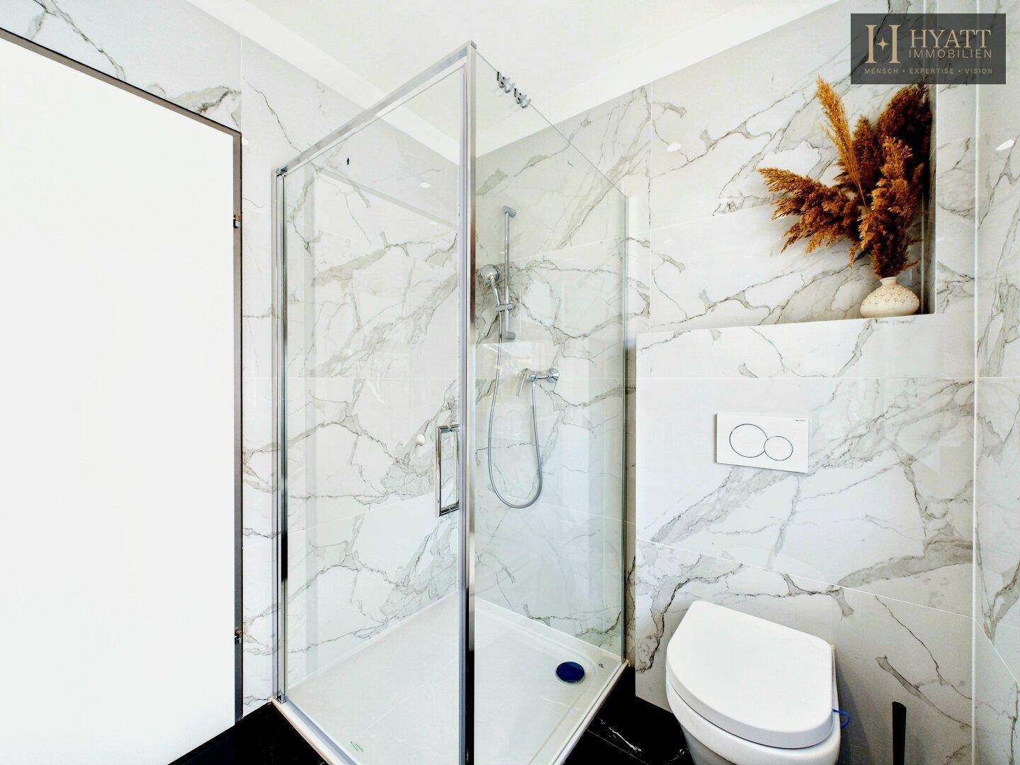 Modernes Badezimmer mit Marmorfliesen, schwarzem Boden und geräumiger Glasdusche.
