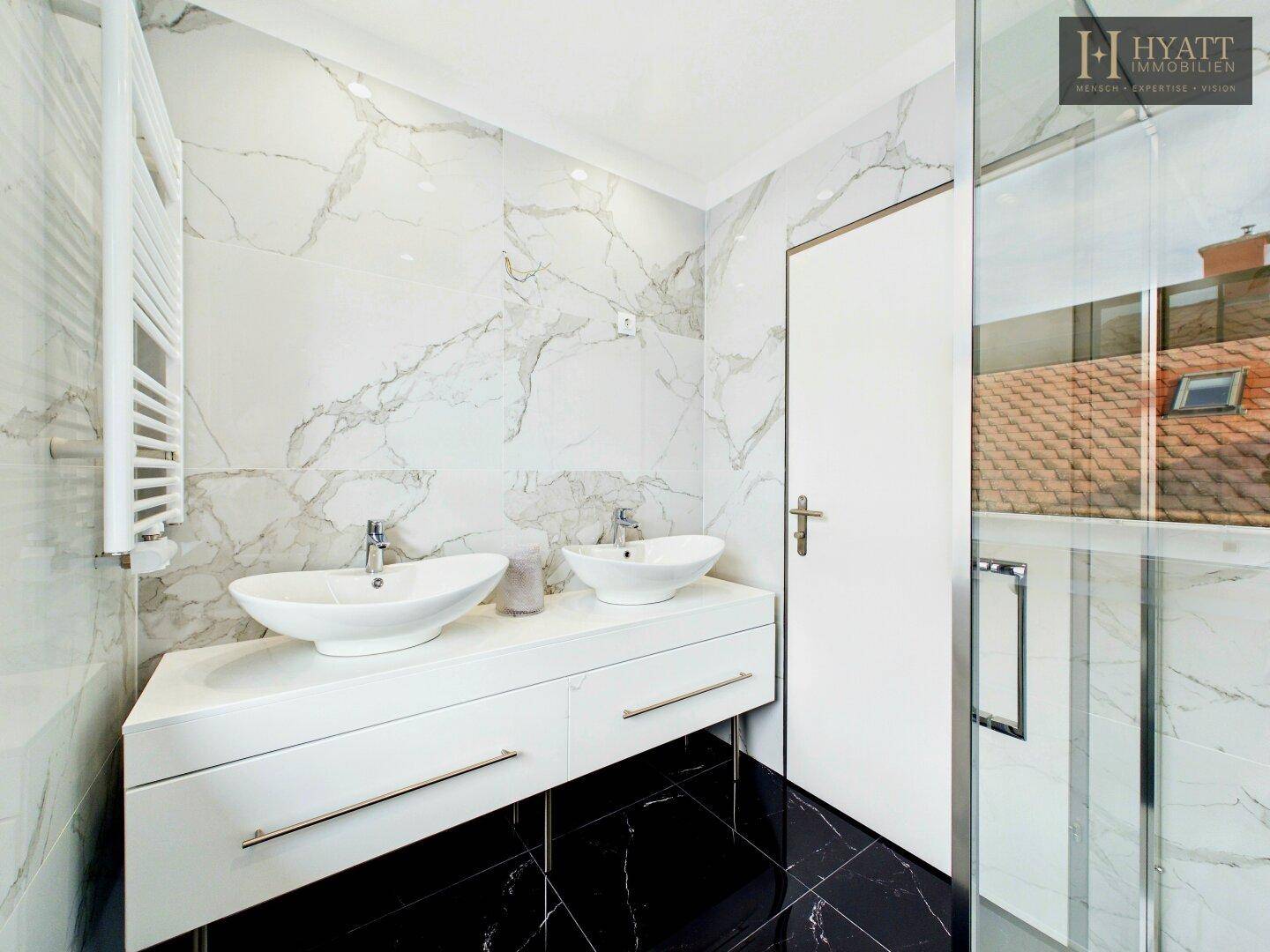 Elegantes Badezimmer mit Doppelwaschbecken, Marmorwänden und schwarzem Fliesenboden.