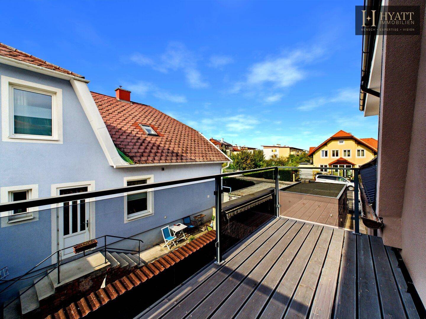 Balkon mit Holzbelag und Glasgeländer bietet einen weiten Blick auf die umliegenden Häuser.