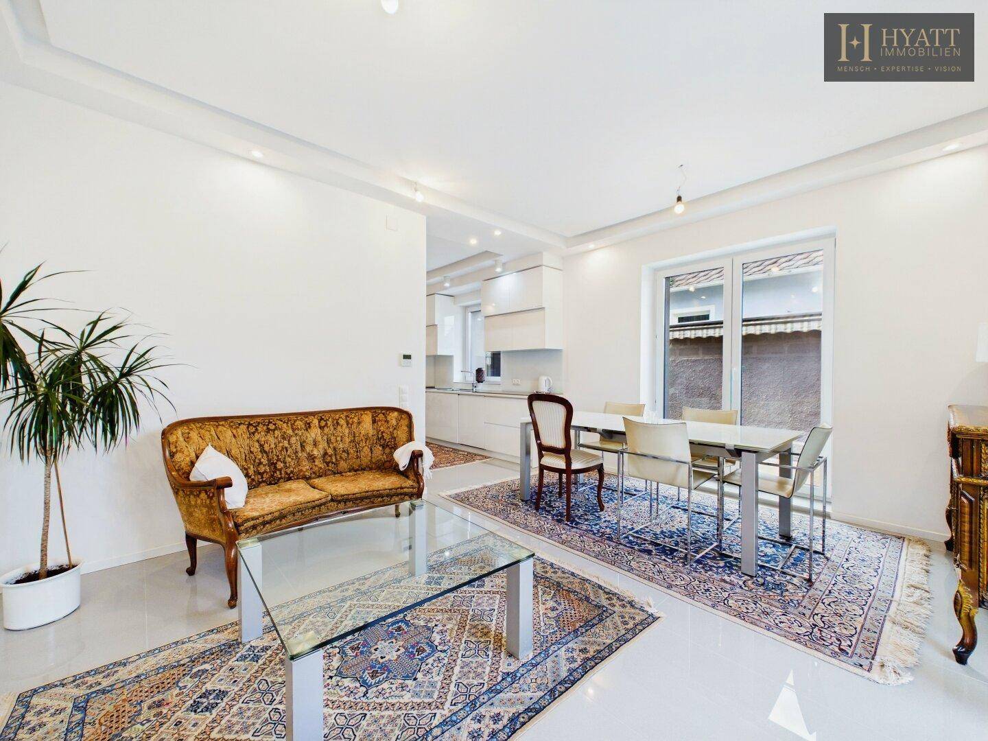 Offener Wohn- und Essbereich mit klassischem Sofa, Teppichen und Blick in die moderne Küche.