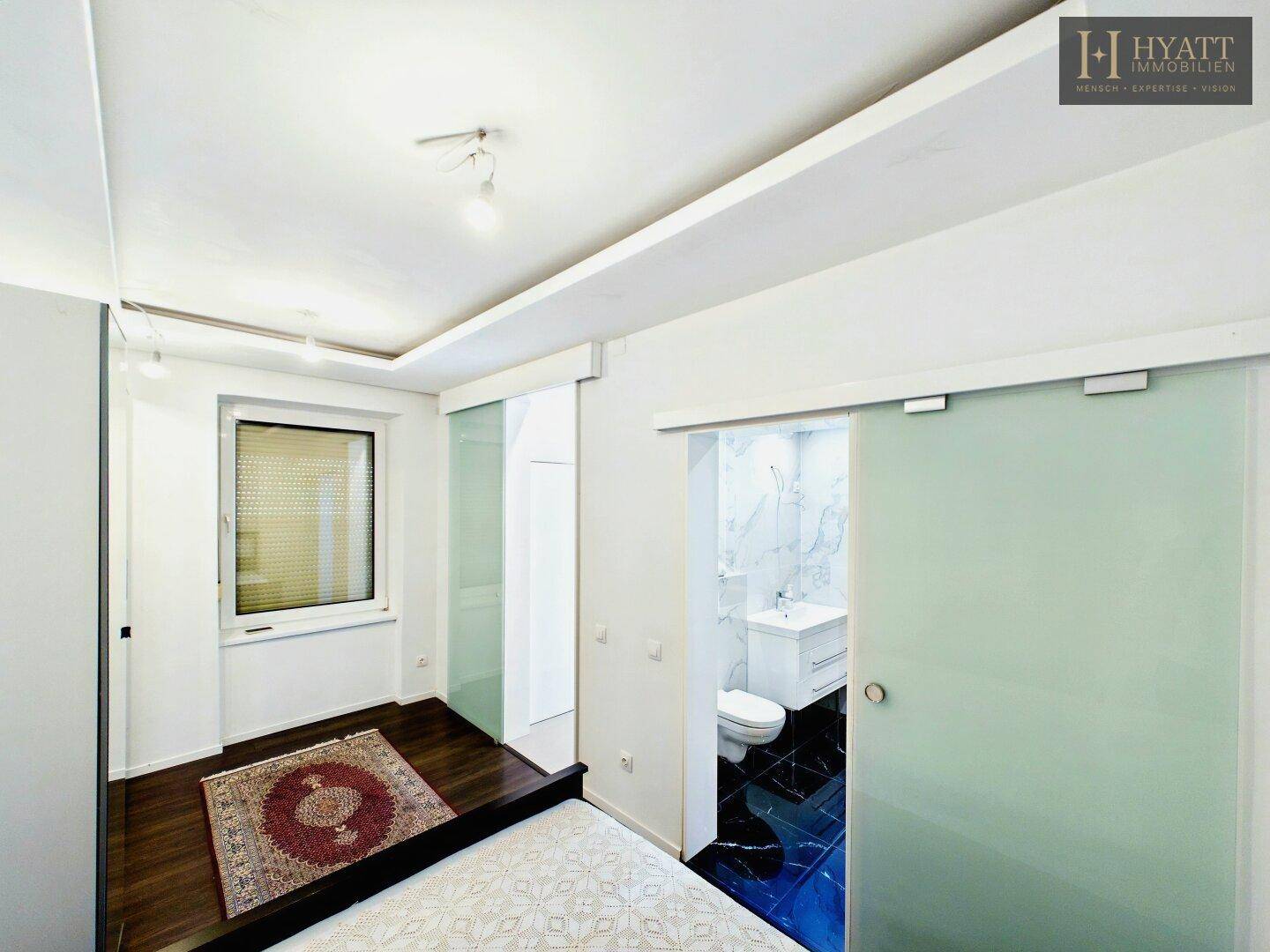 Helles Schlafzimmer mit Holzboden, Fenster und Schiebetür zum modernen Badezimmer.